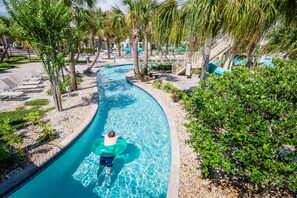 Une piscine à eau claire, de forme incurvée, entourée de palmiers et de chaises longues.