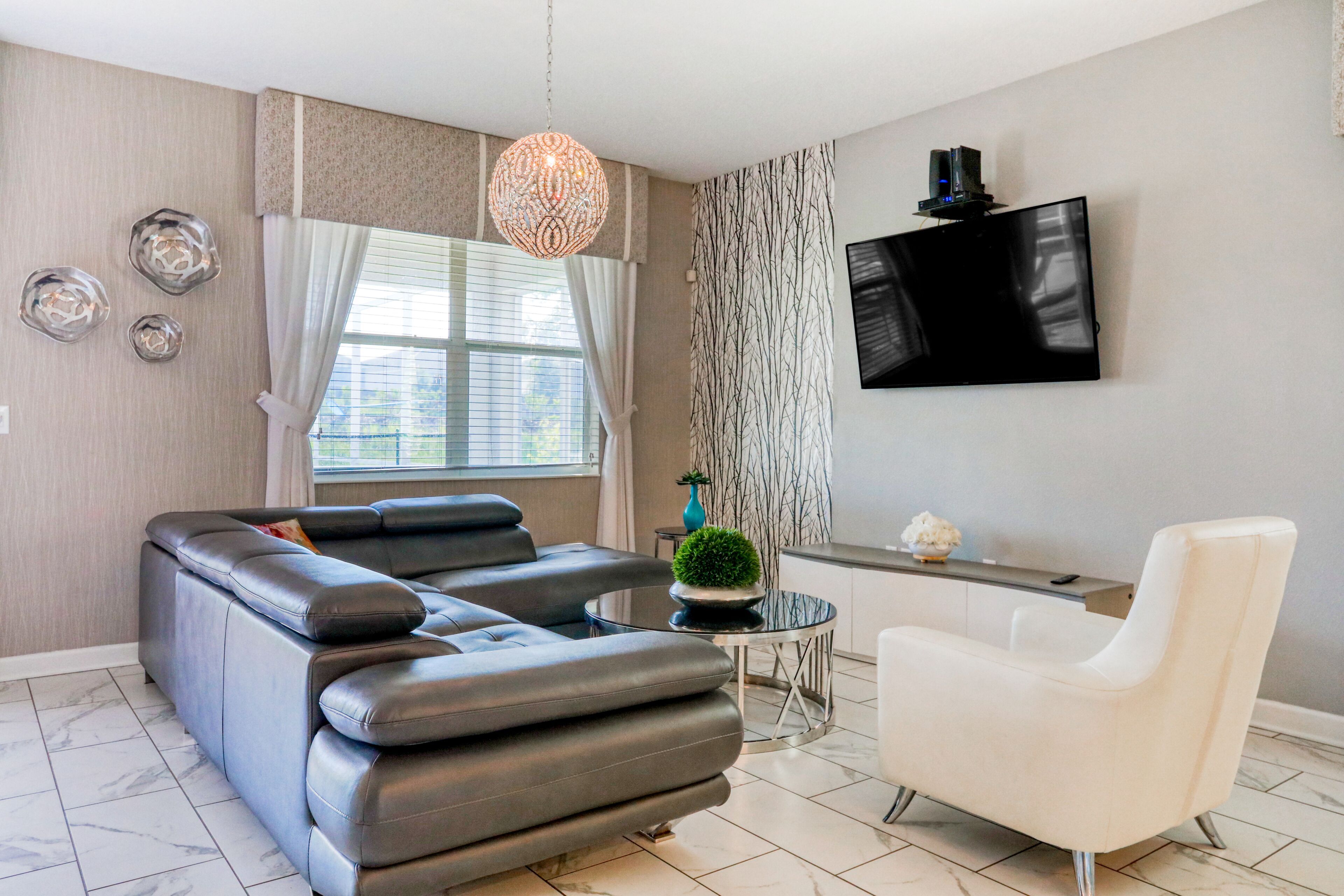 Een moderne woonkamer met een leren bank, een witte fauteuil, een ronde salontafel en een flatscreen televisie aan de muur.