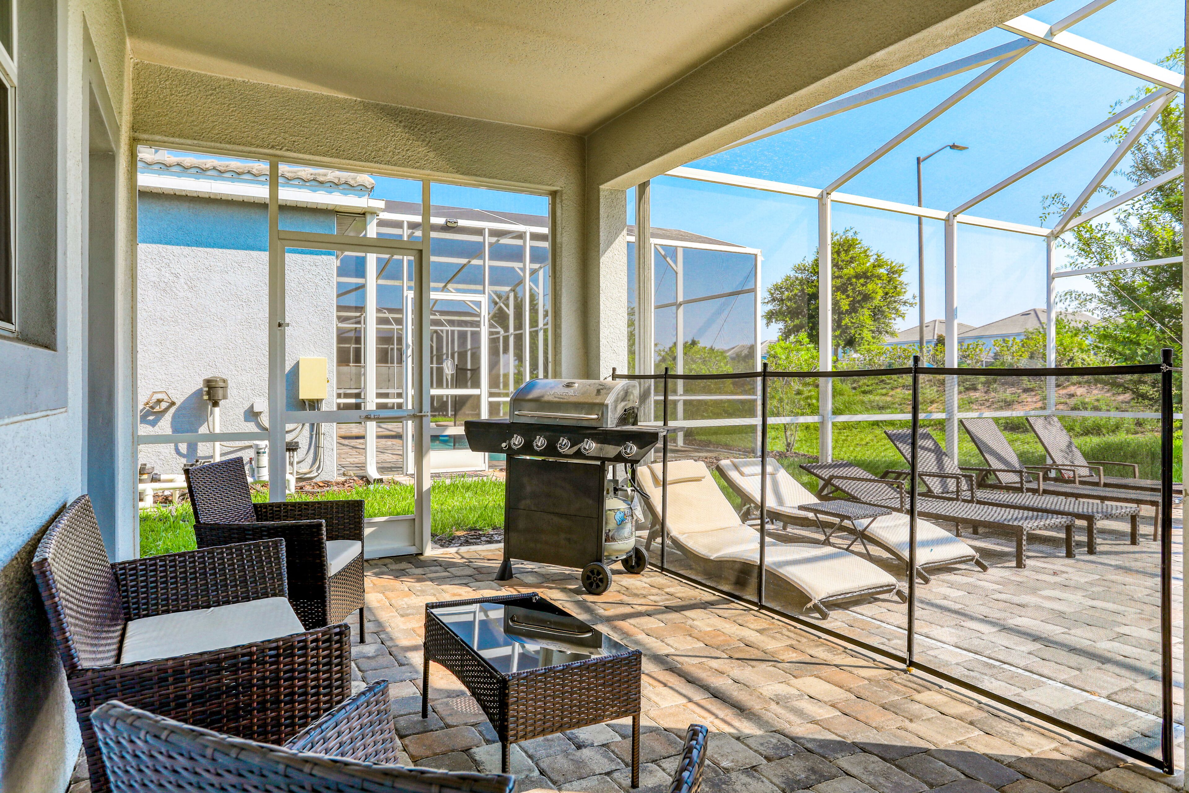An outdoor patio with wicker furniture, a grill, and a glass enclosure offering a view of the backyard.