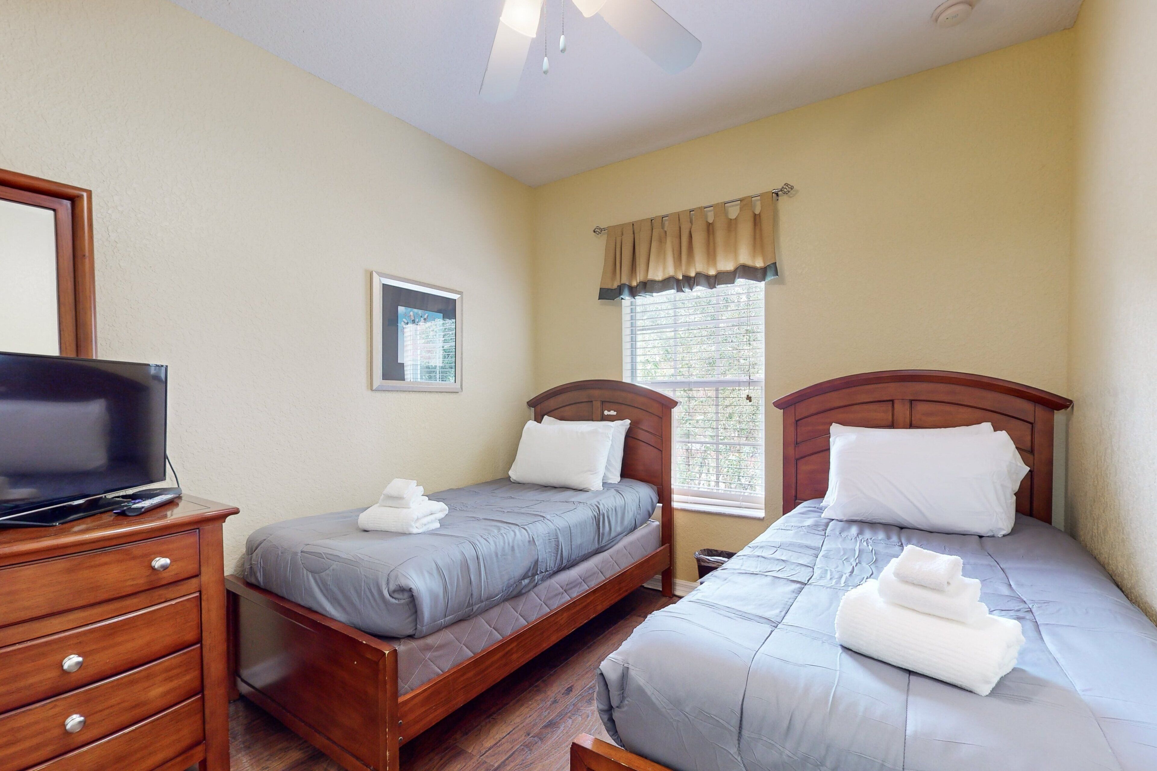 A bedroom with two beds, a TV, wooden furniture, and a window with curtains.