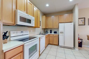 A kitchen with wooden cabinets, a white microwave, stove, dishwasher, and refrigerator. - Gated-entry Townhome, With Shared Pool, Central AC, Near Theme Parks (Kissimmee)