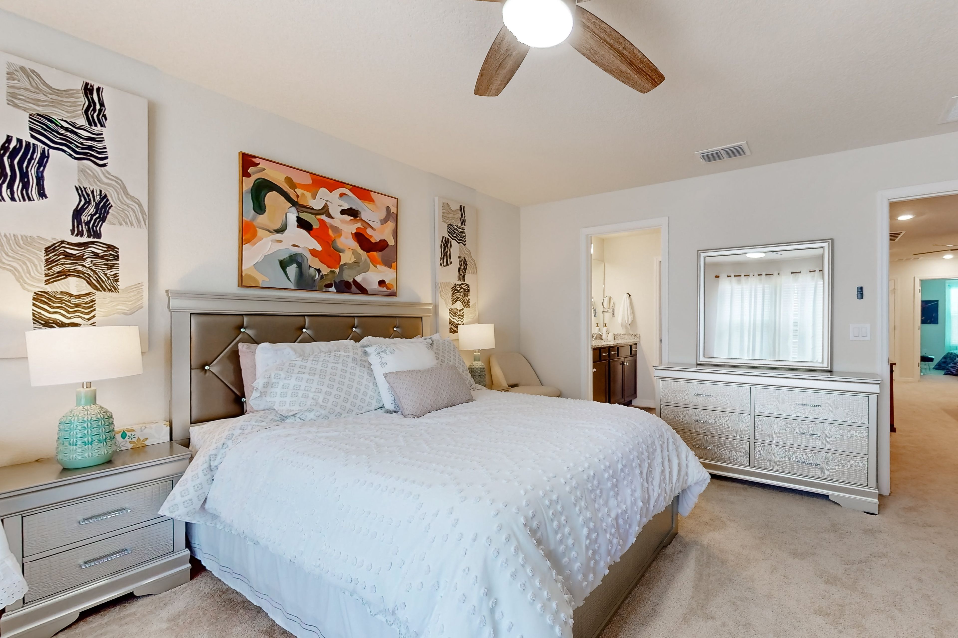 A bedroom with a bed, nightstands, a dresser, a ceiling fan, and artwork on the walls.