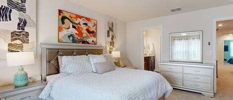 A bedroom with a bed, nightstands, a dresser, a ceiling fan, and artwork on the walls.