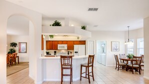A spacious kitchen with wooden cabinets, a white island, and a dining area with wooden chairs. - Gorgeous Home Near Disney With Private Pool, Pool Spa, On-site Gym, Tennis, AC (Davenport)