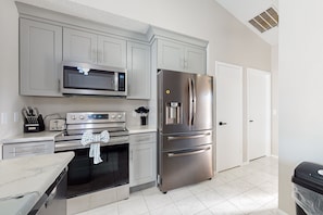 A modern kitchen with stainless steel appliances, grey cabinets, and a tiled floor. - Spacious Dog-friendly Home W/private Pool, Pong Pong, Near Disney (Kissimmee)