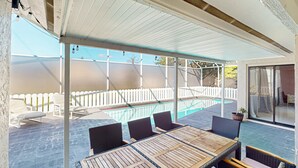 Uma área externa coberta com piscina, espreguiçadeiras e uma mesa com cadeiras.