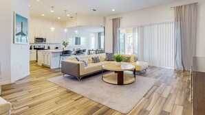 A modern living room with a sofa, coffee table, and kitchen in the background. - Spacious, Lakefront Home With a Lanai, Private Pool, Spa, & Washer/dryer (Davenport)