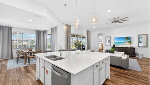 A modern kitchen with a central island, a dining area with a table and chairs, a living room with a sofa and TV, and a ceiling fan. - Spacious, Lakefront Home With a Lanai, Private Pool, Spa, & Washer/dryer (Davenport)