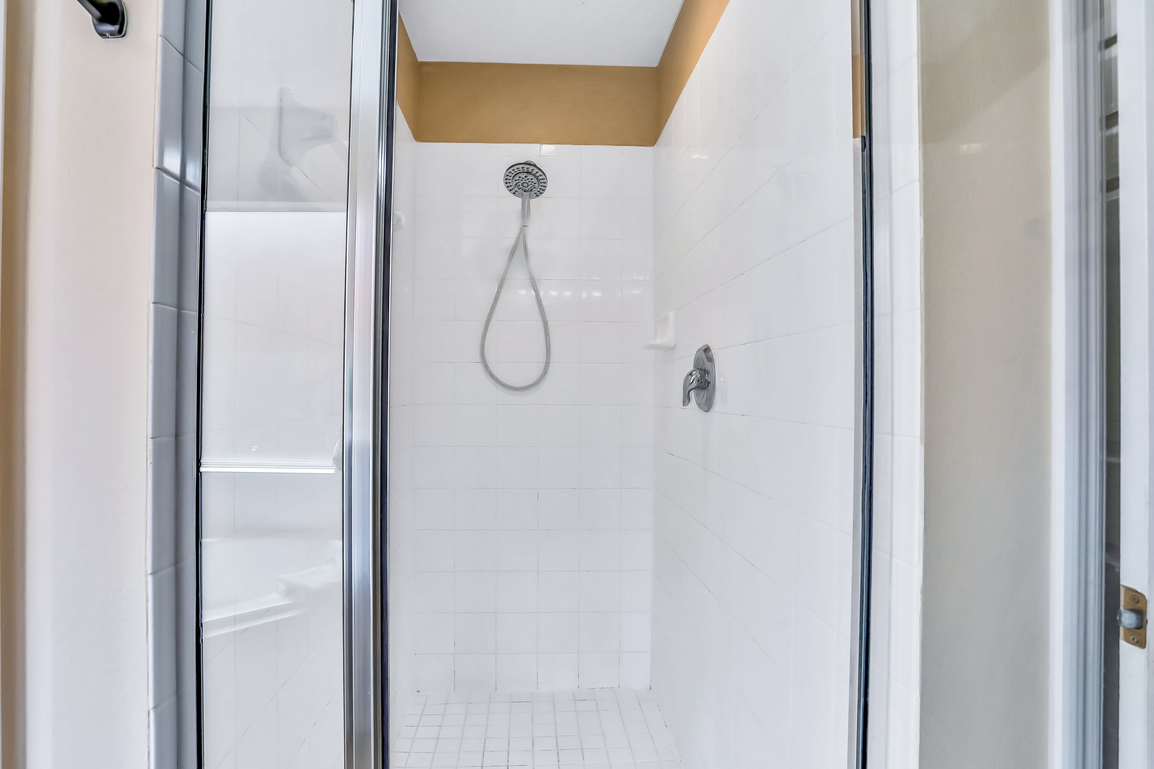 A modern shower with a glass door, white tiled walls, and a beige ceiling.