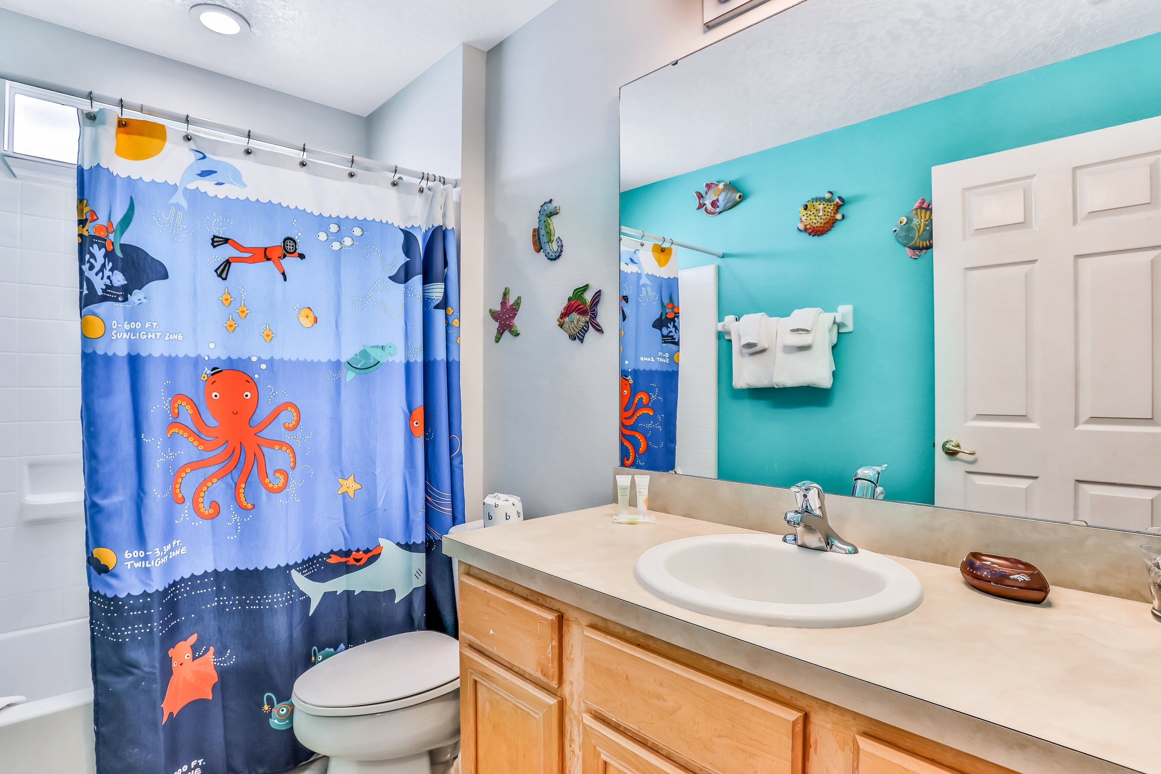 A bathroom with a shower curtain featuring sea creatures, a sink with a mirror, and a toilet.