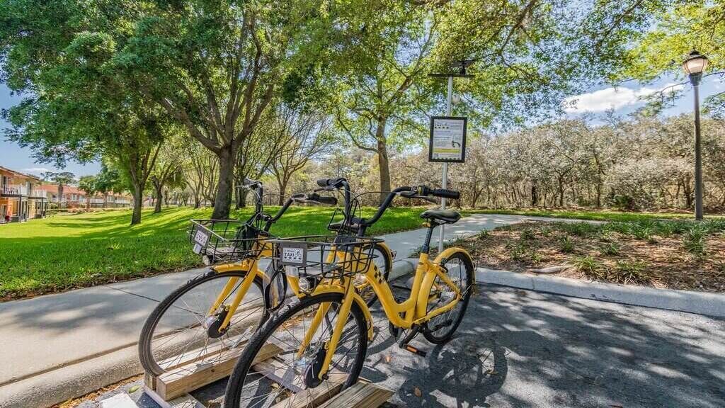 Een gele fiets geparkeerd op een stoep met een bordje op de achtergrond.