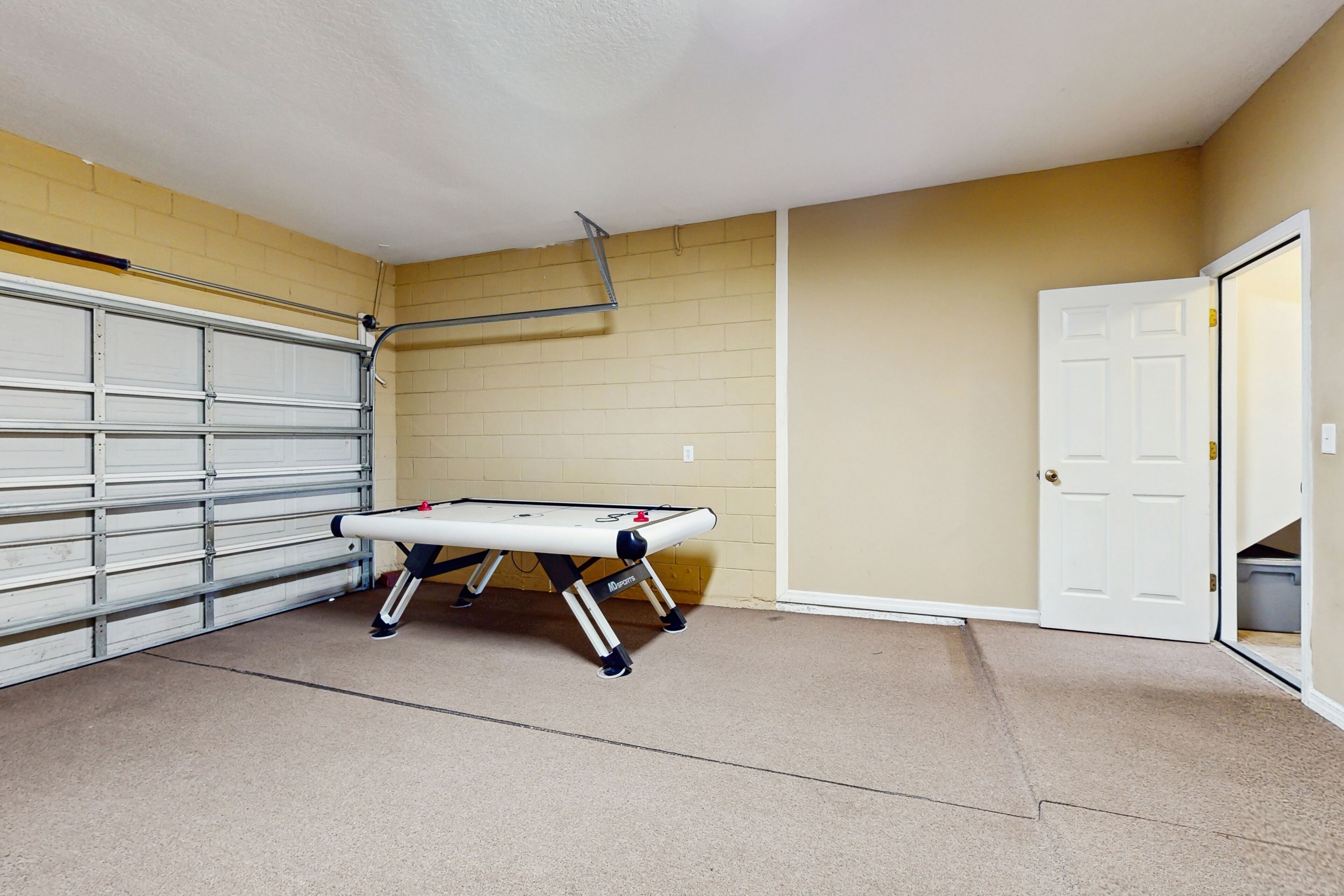A garage with a pool table, a white door, and beige walls.