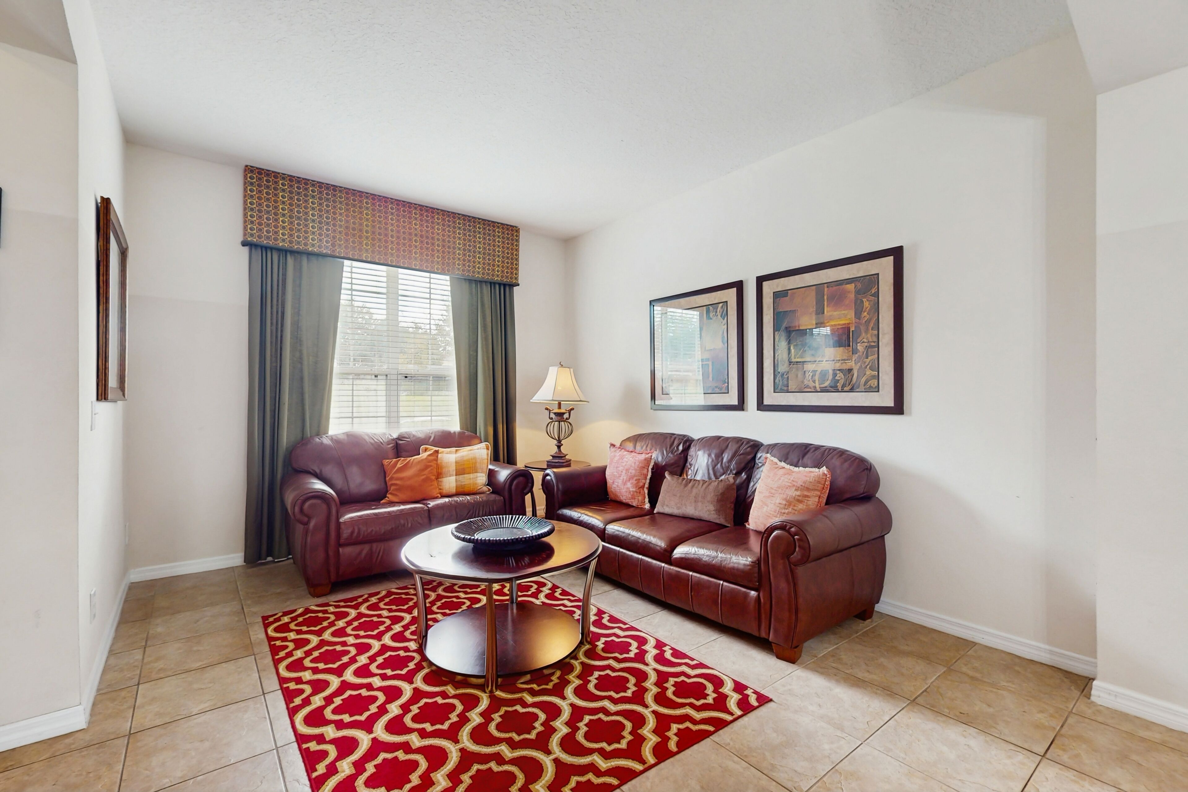 A living room with two leather sofas, a coffee table, a patterned rug, and two framed artworks on the wall.