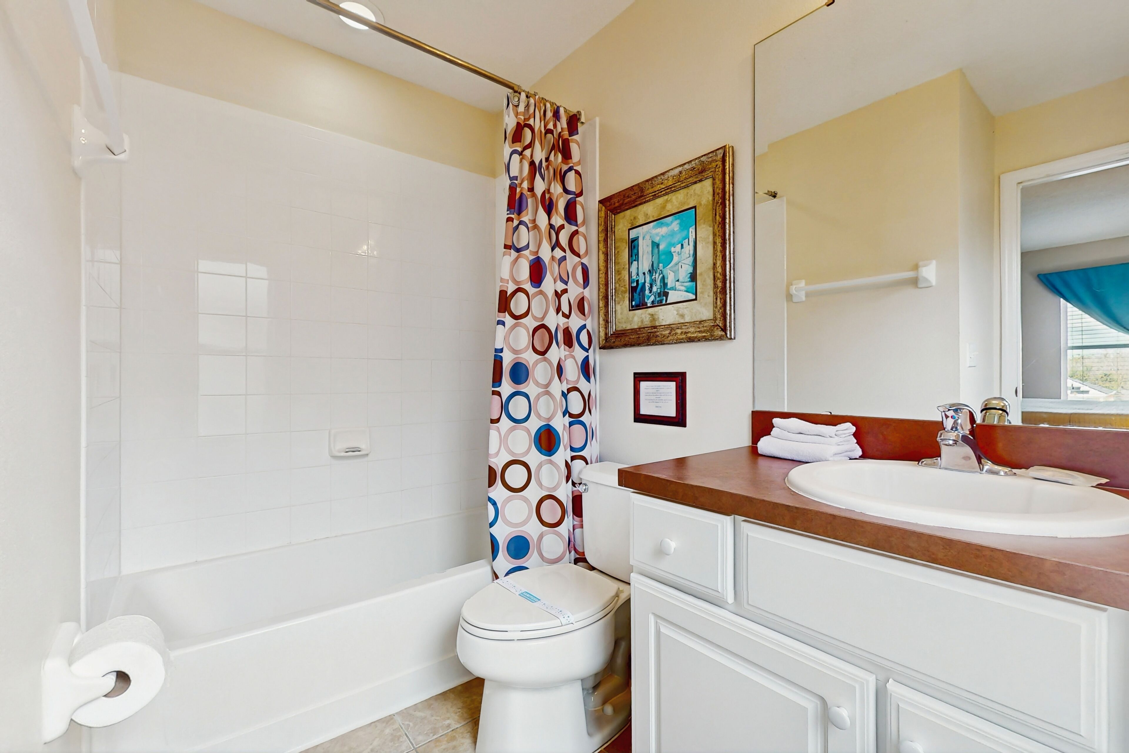 Ein Badezimmer mit Toilette, Badewanne, Waschbecken mit Spiegel und einer Duschvorhang mit Rundmuster.