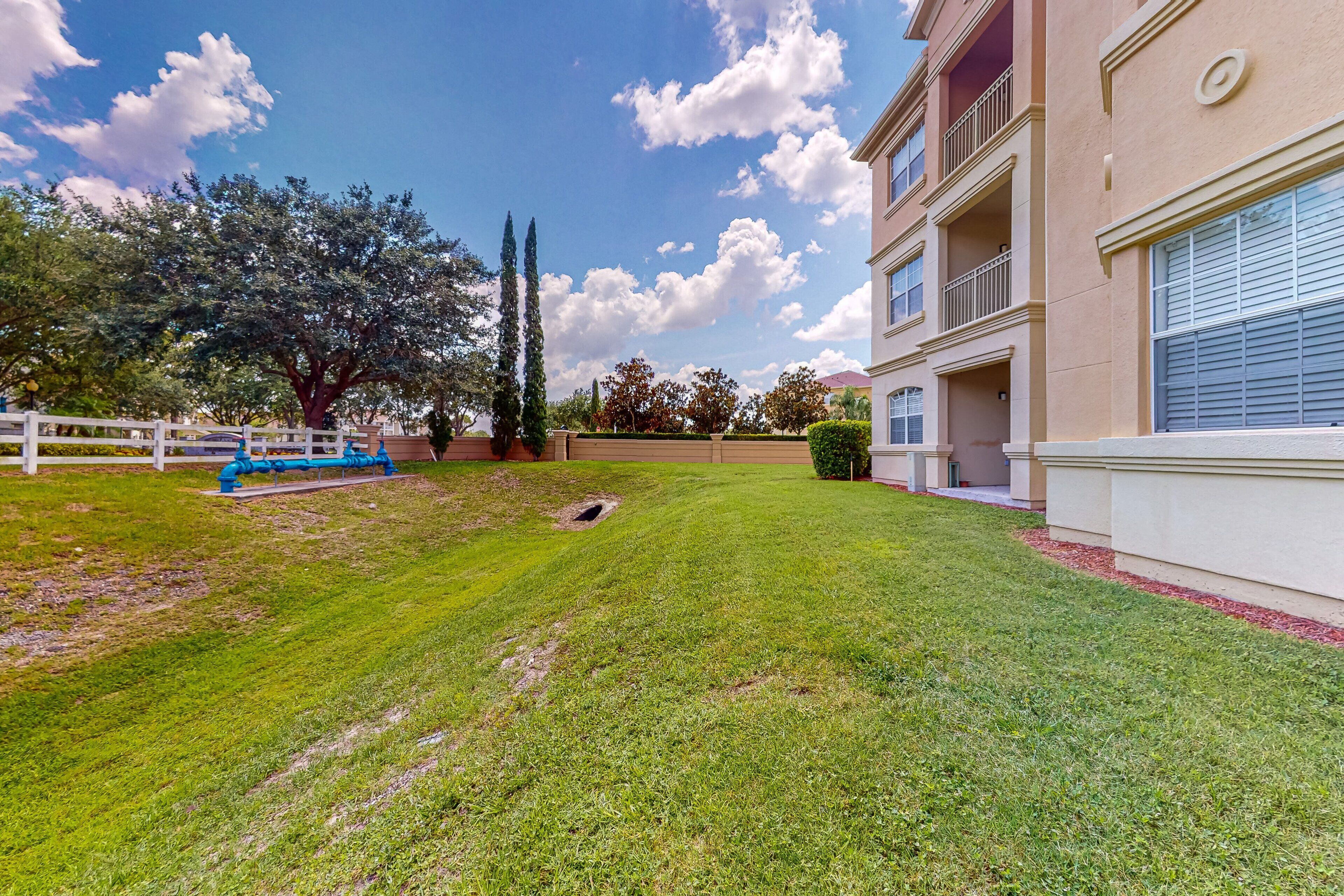 A well-maintained lawn, a white fence, and a multi-story building with balconies.