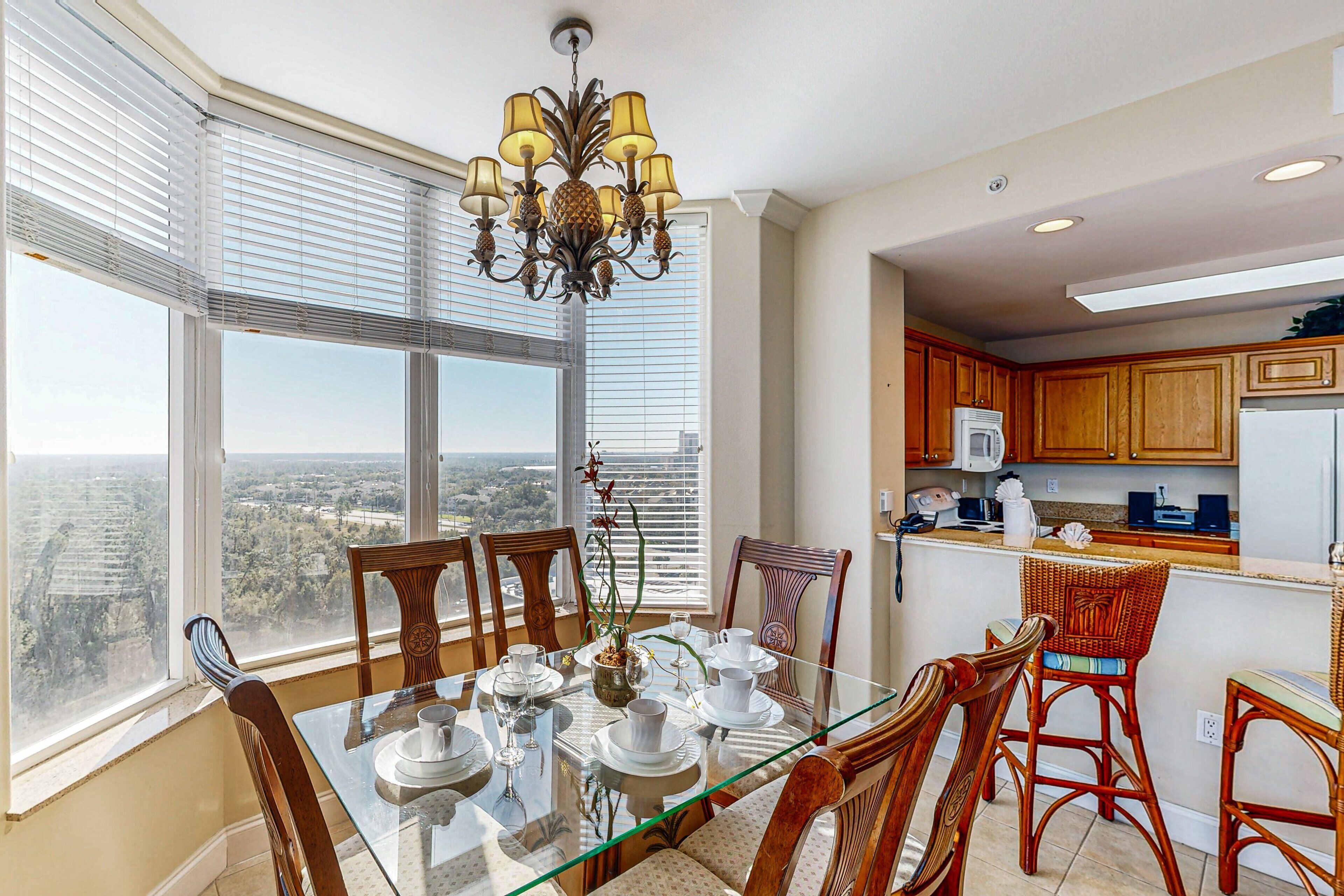 A dining area with a glass table, chairs, and a view through large windows.