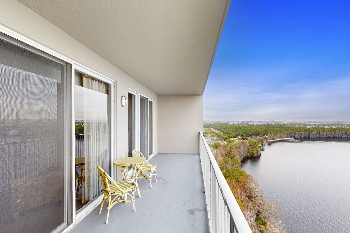 A balcony with a table and chairs, overlooking a body of water and a distant shoreline.