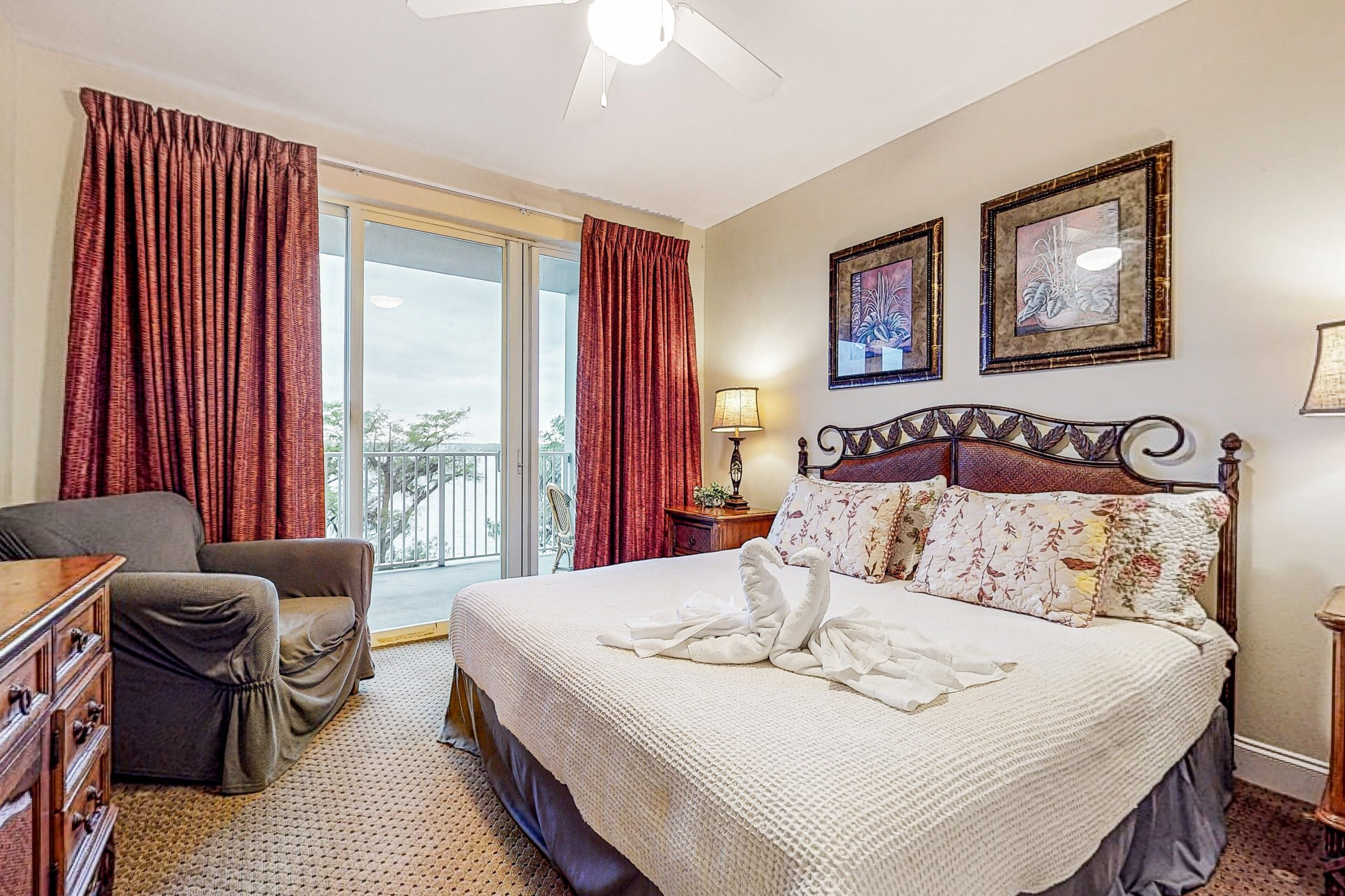 A hotel room with a bed, a chair, a desk, a lamp, and a balcony with curtains.