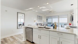 A modern kitchen with white cabinetry, a dishwasher, and a large window providing a view. - Blue Heron Beach II (Orlando)