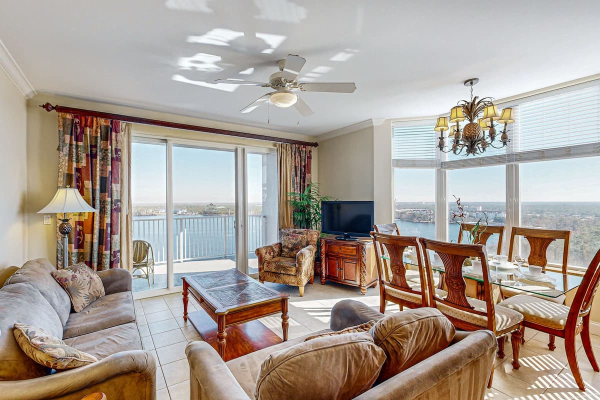 A spacious living room with a sofa, armchairs, a coffee table, a TV, and a dining area with chairs and a chandelier.