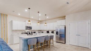A modern kitchen with white cabinets, a stainless steel refrigerator, and a central island with bar stools. - Spacious Private Home w/ Private Pool, Resort Style Waterpark & Mini Golf Access (Davenport)