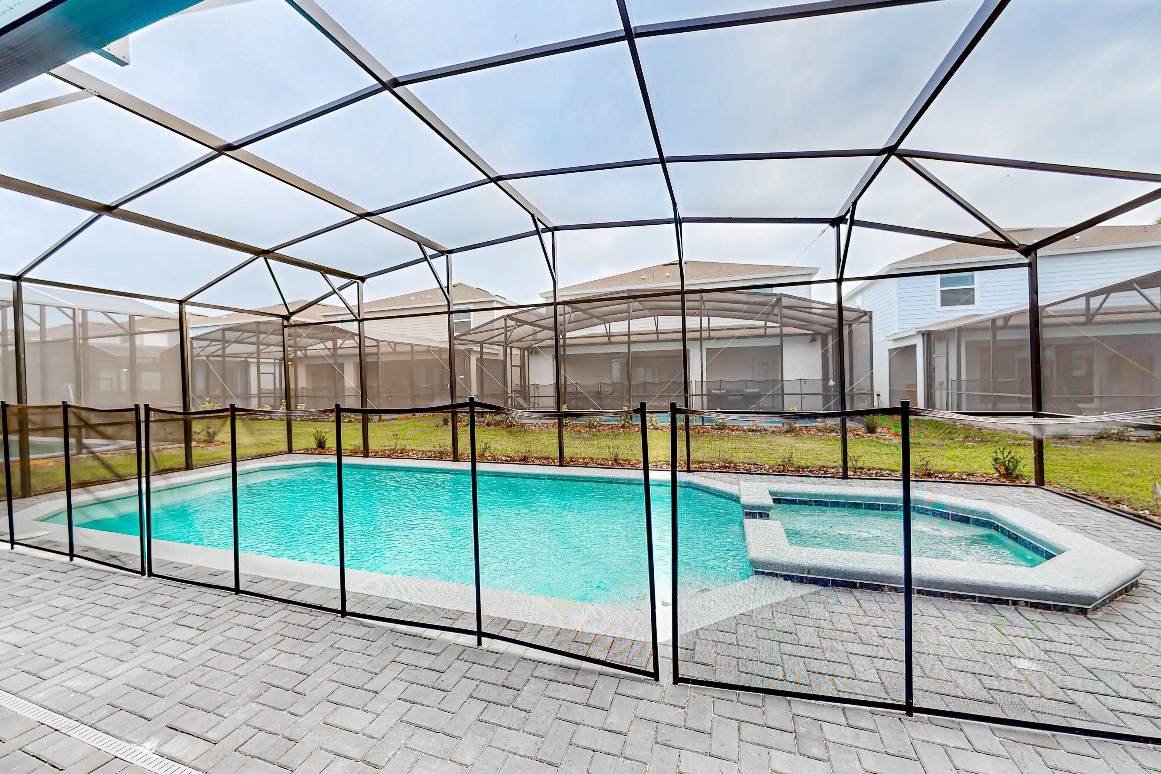 A swimming pool enclosed by a transparent safety fence, with a brick patio surrounding it.