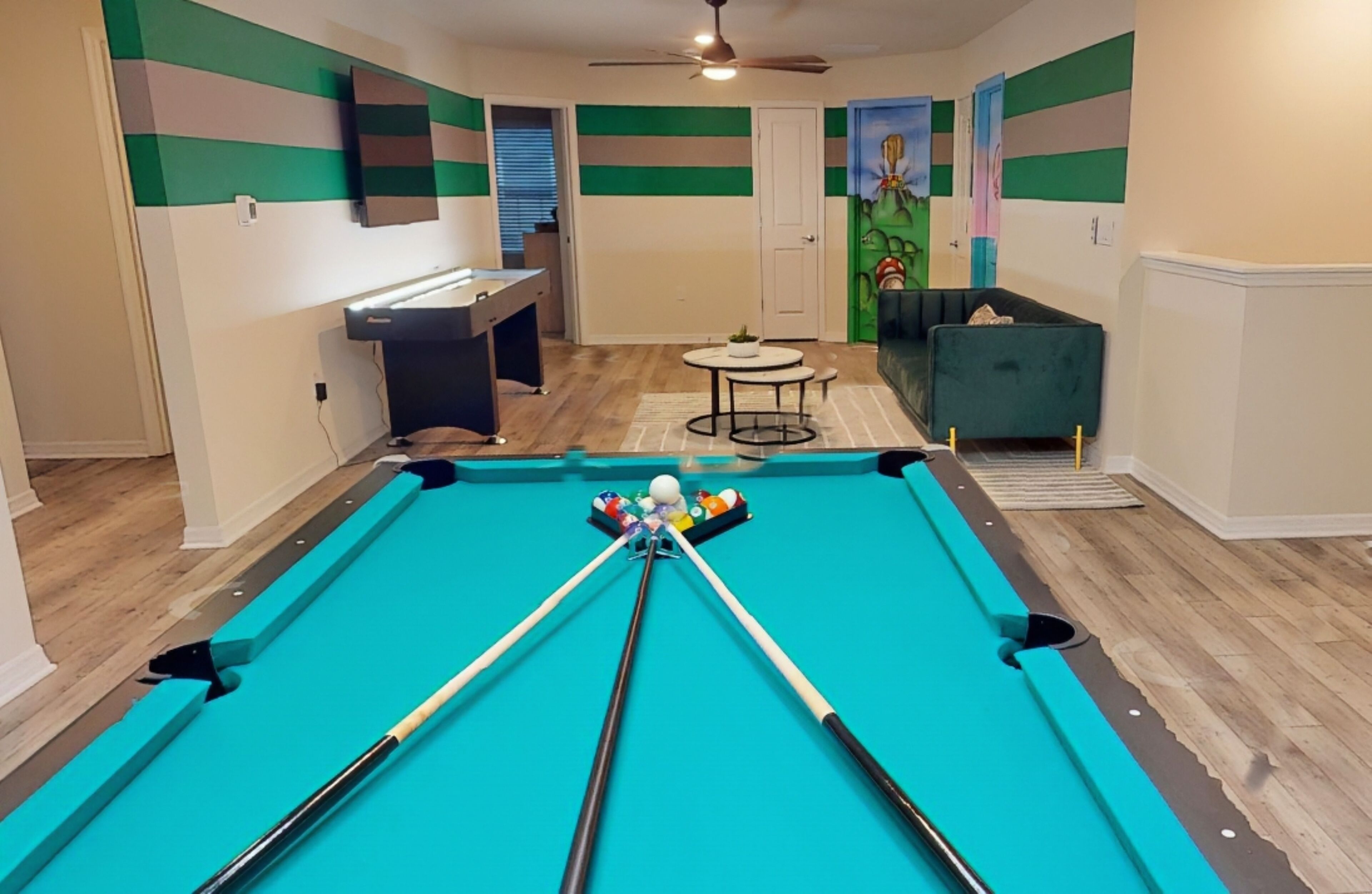 A pool table with pool cues and balls, a ceiling fan, and a small table with a plant.