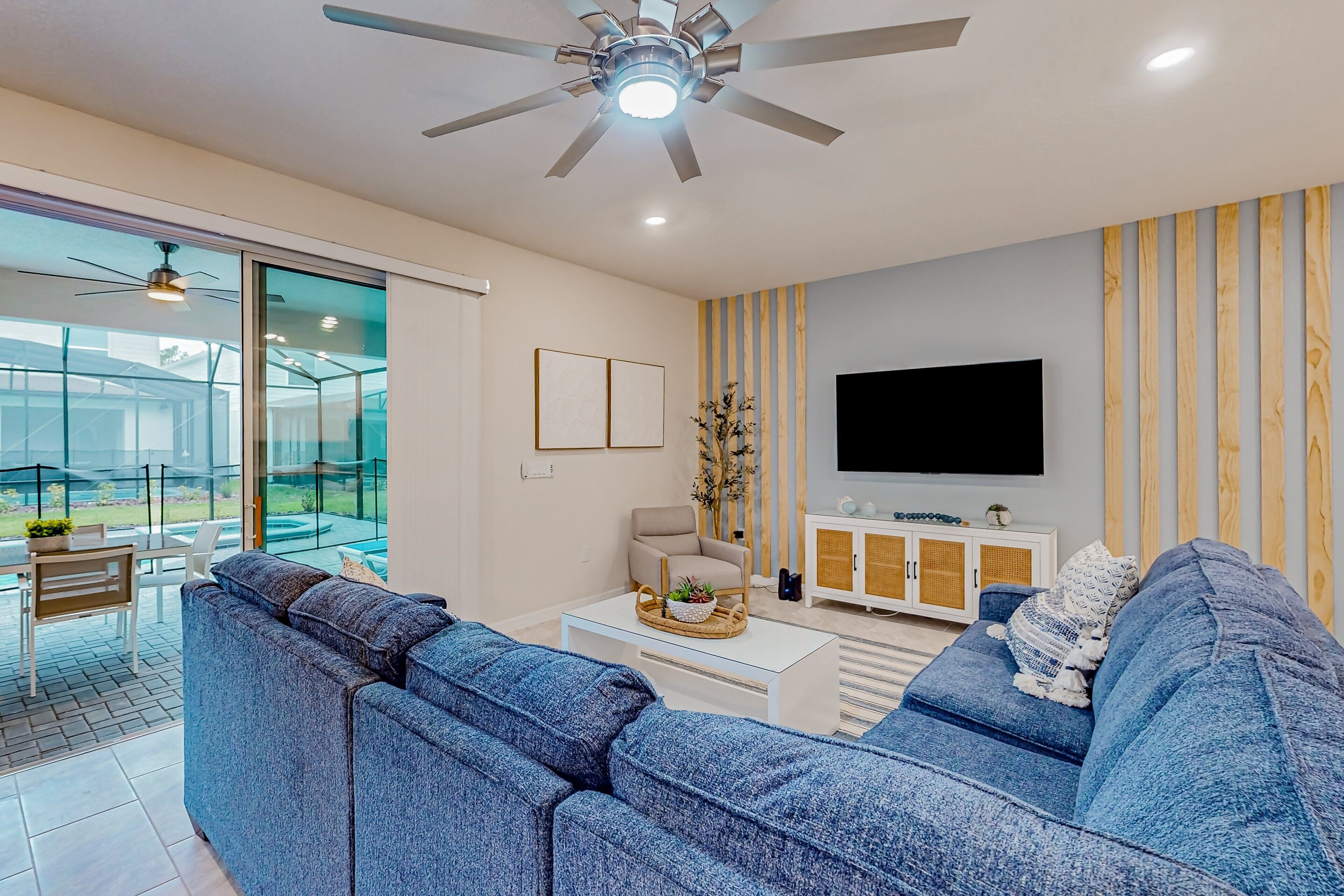 A modern living room with a large blue sectional sofa, a white coffee table, a beige armchair, and a TV mounted on the wall.