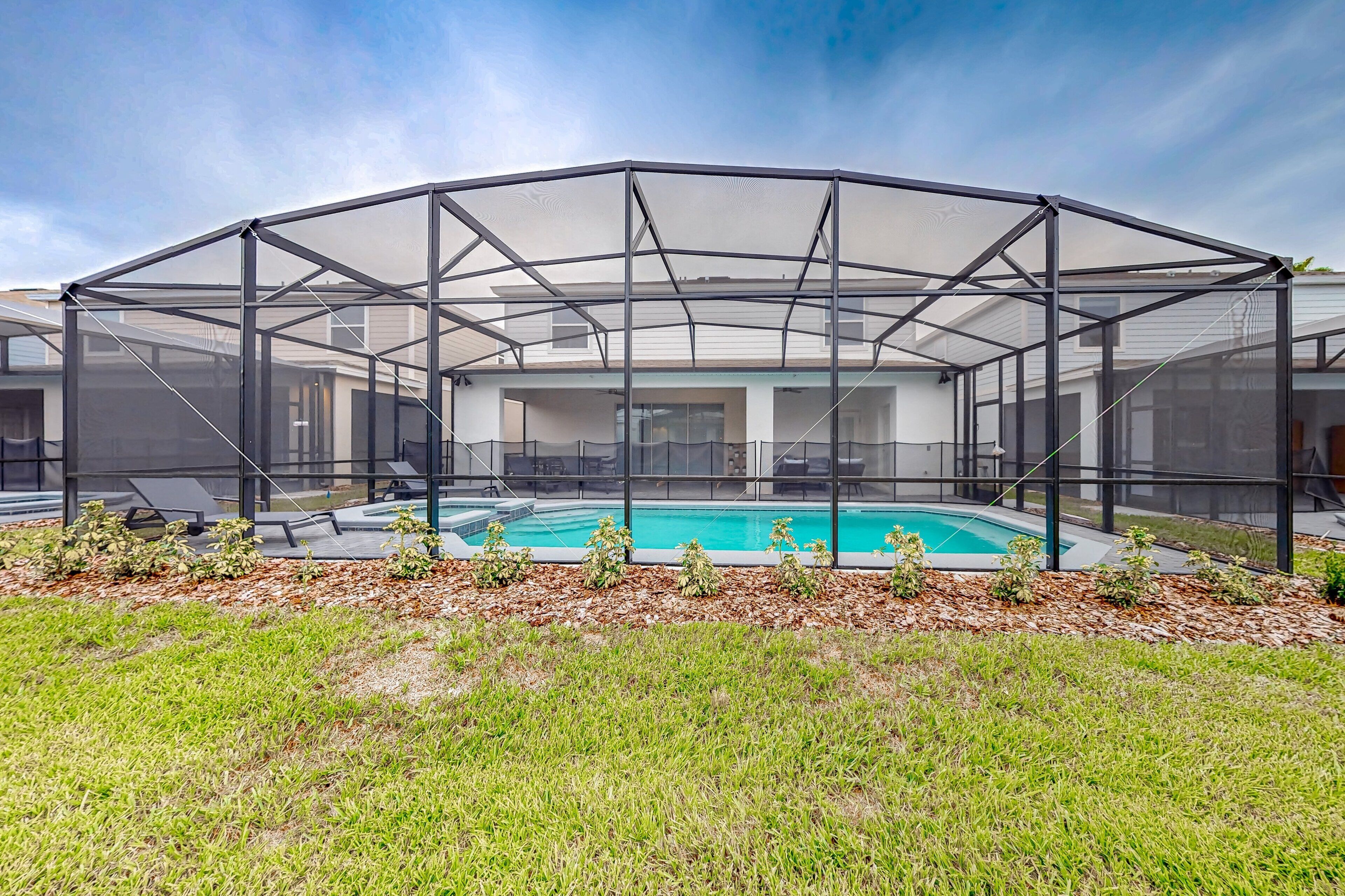 A covered outdoor swimming pool with a metal frame and mesh sides, surrounded by grass and plants.