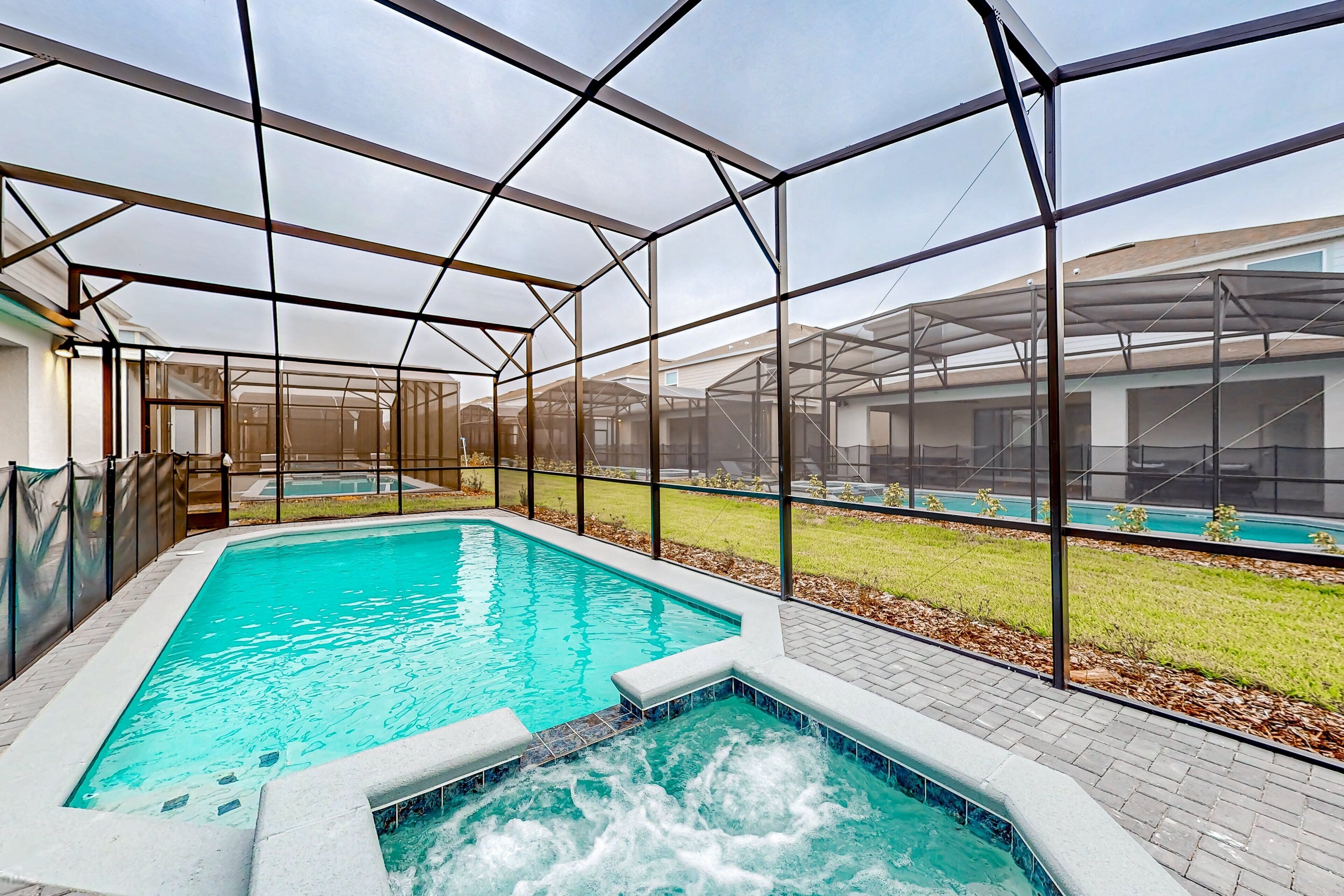 Piscina con bañera de hidromasaje, rodeada por un recinto de vidrio con vistas a un área verde y un edificio al fondo.