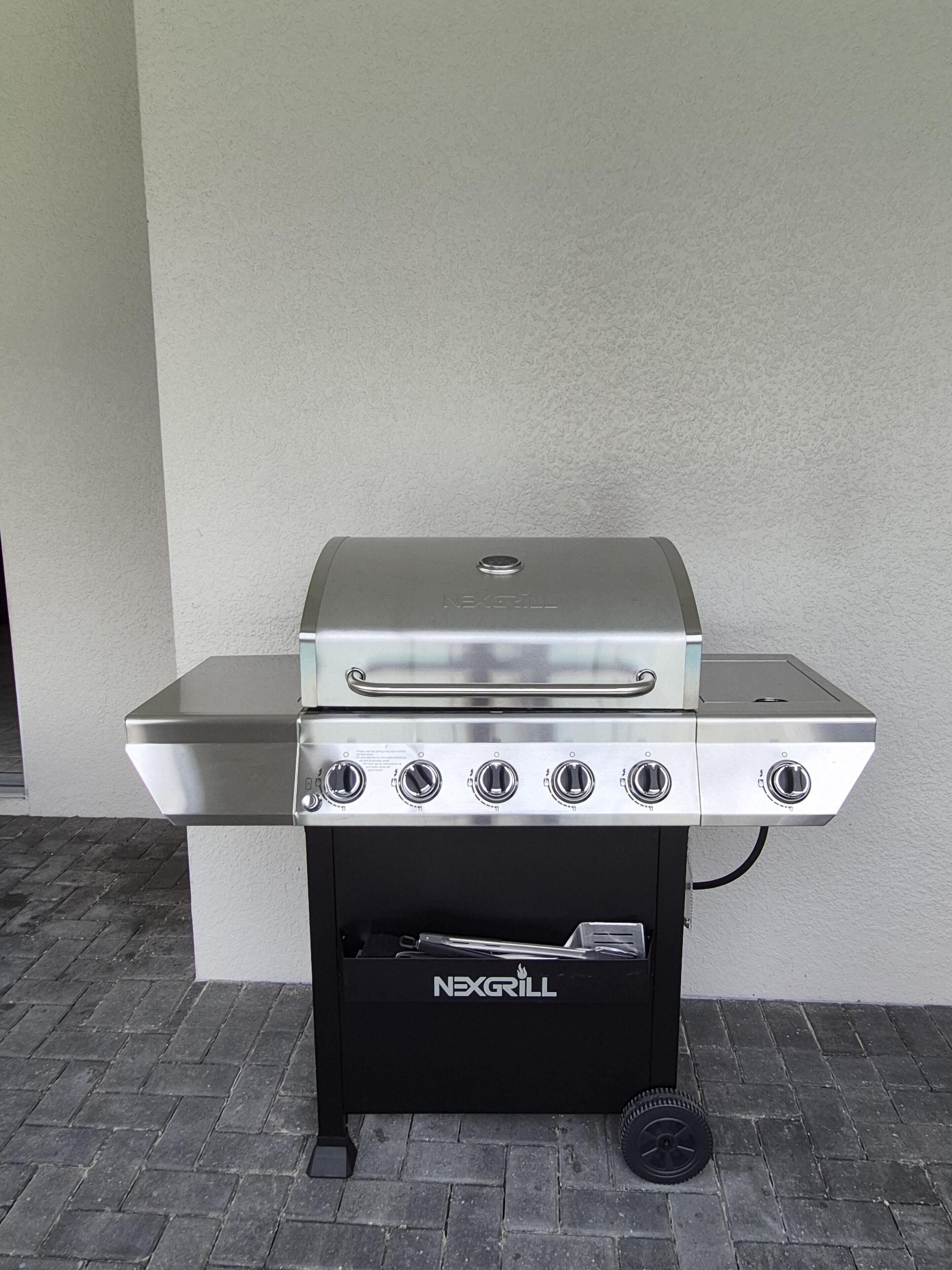 Una barbacoa NEXGRILL amb acabat d'acer inoxidable, un panell de control amb cinc comandaments i una base negra amb rodes.