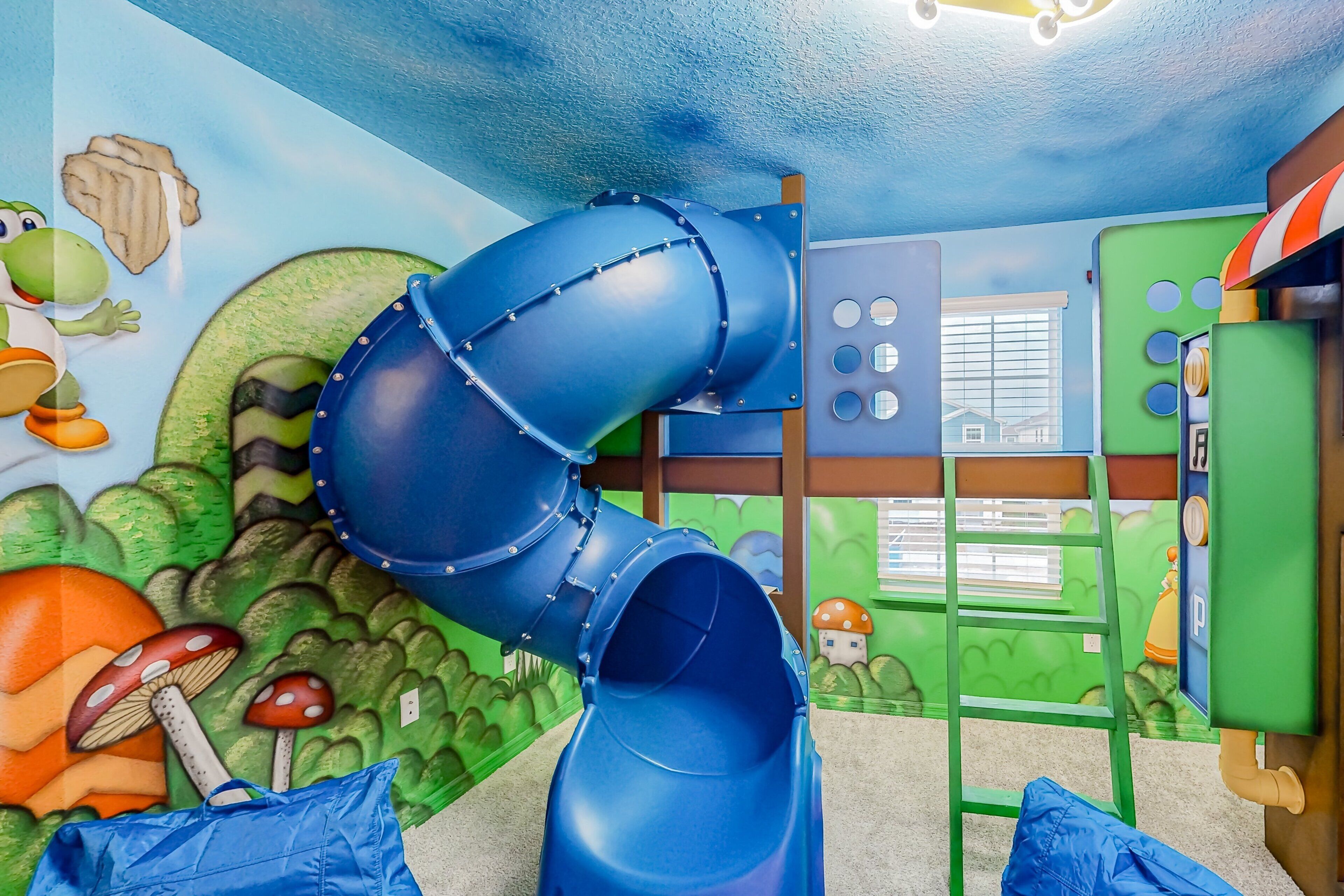 A children's play area with a blue slide, a green climbing wall, and a mural with mushrooms and a character.