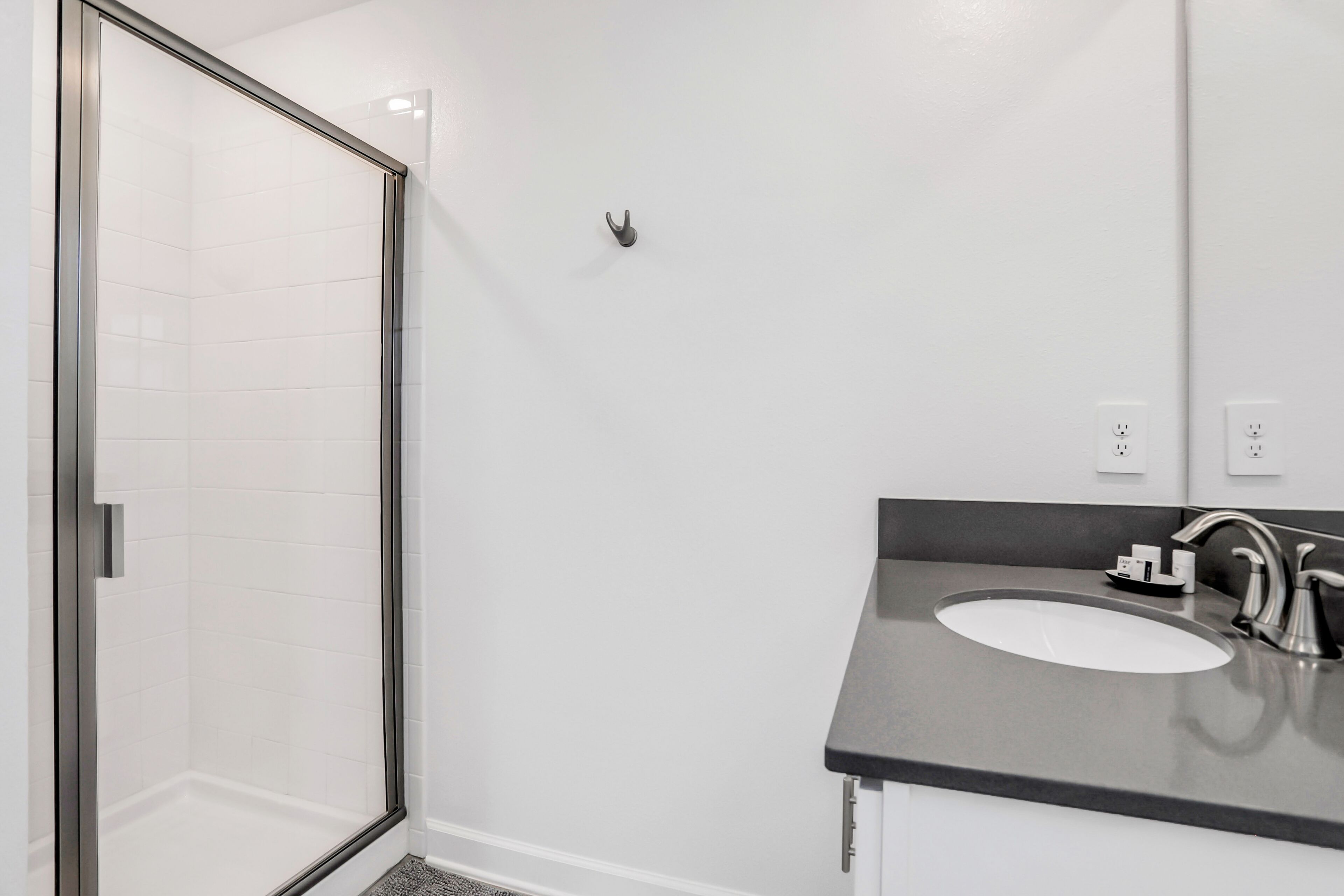 Une salle de bain moderne avec une douche à l’italienne en verre, un lavabo blanc doté d’un plan de toilette foncé et un grand miroir.
