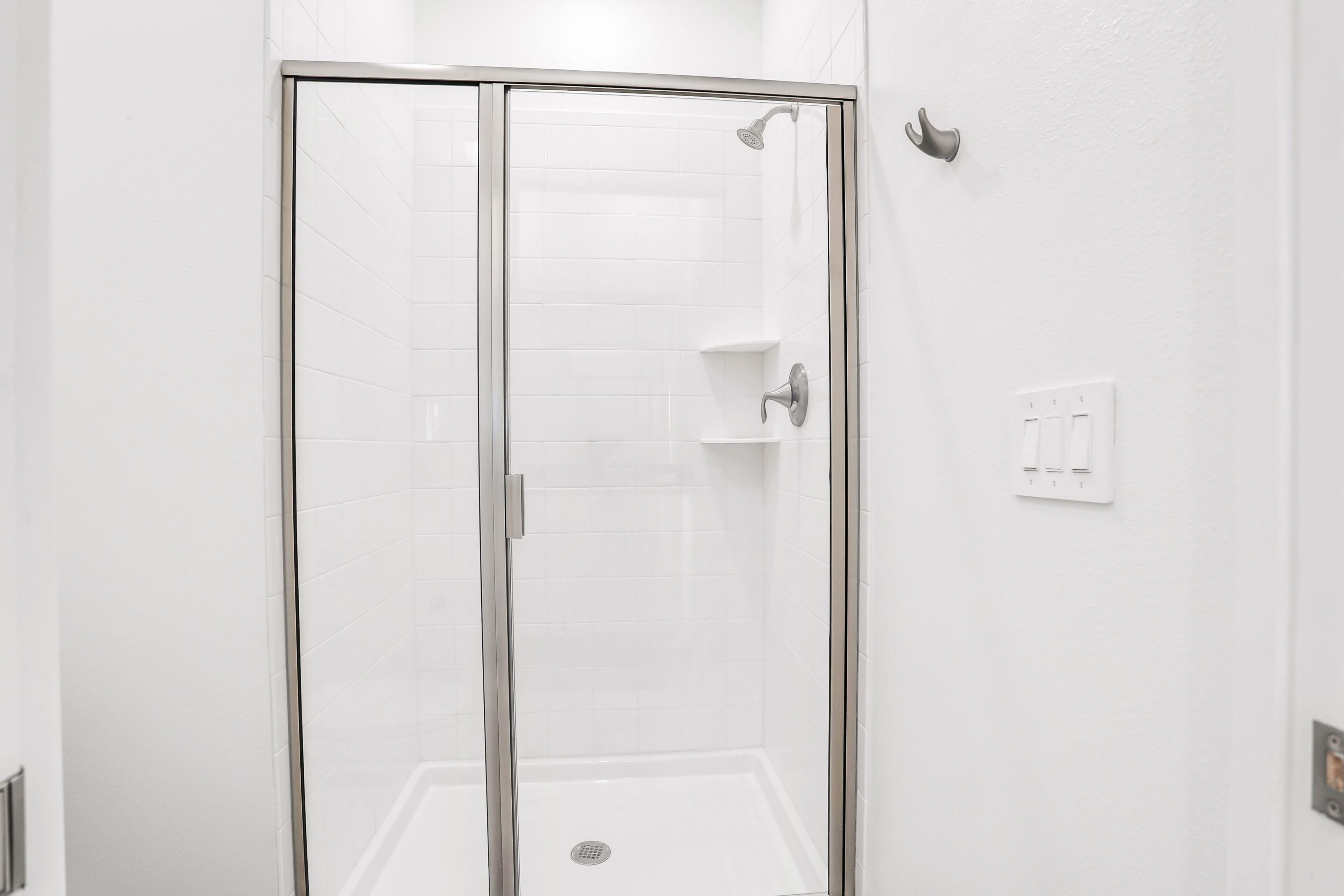 A glass-enclosed shower with a white tiled wall, a wall-mounted towel rack, and a light switch.
