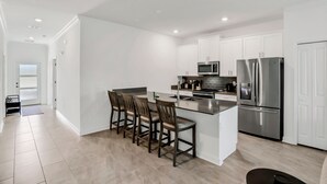 A modern kitchen with white cabinetry, stainless steel appliances, and a central island with bar stools. - Updated Townhome With an Enclosed Pool, Five Bedrooms, W/D - Close to Everything (Kissimmee)