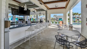 A covered outdoor bar area with a pool view, white bar stools, and ceiling fans. - Updated Townhome With an Enclosed Pool, Five Bedrooms, W/D - Close to Everything (Kissimmee)