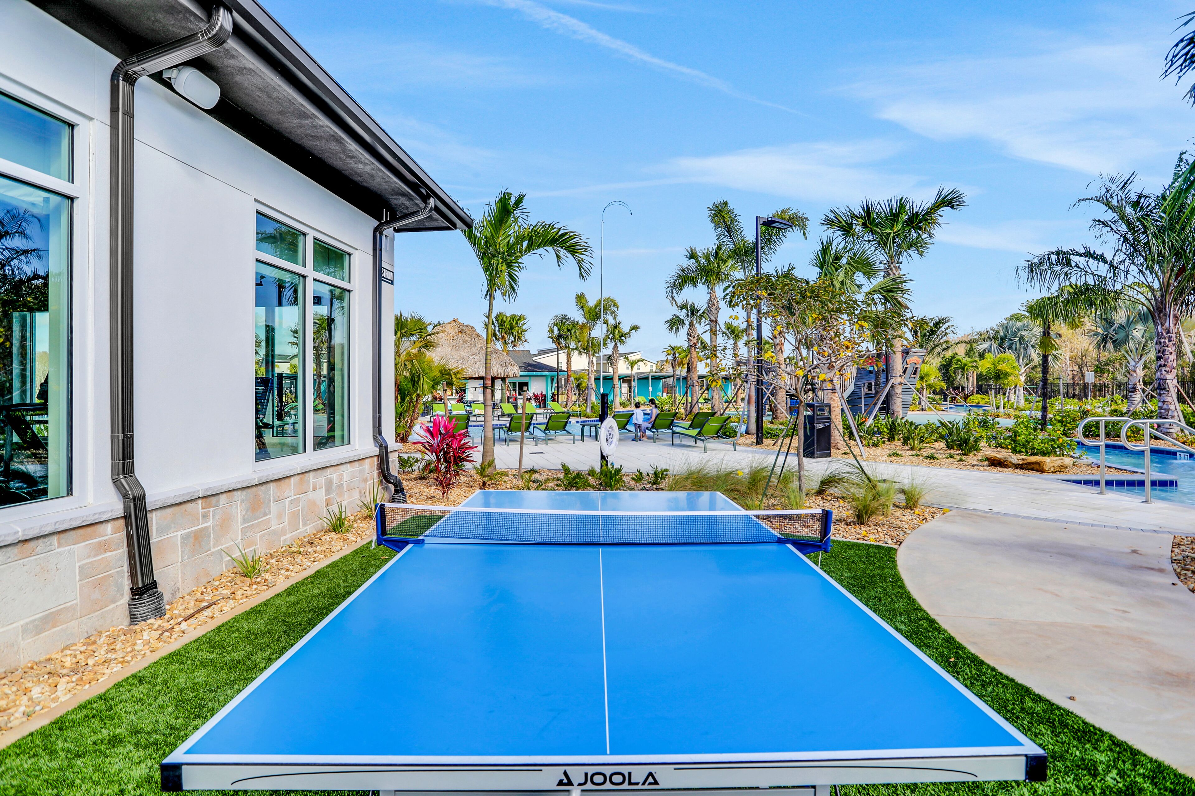 Ein Tischtennis-Tisch in einem Außenbereich mit Palmen und einem Pool im Hintergrund.