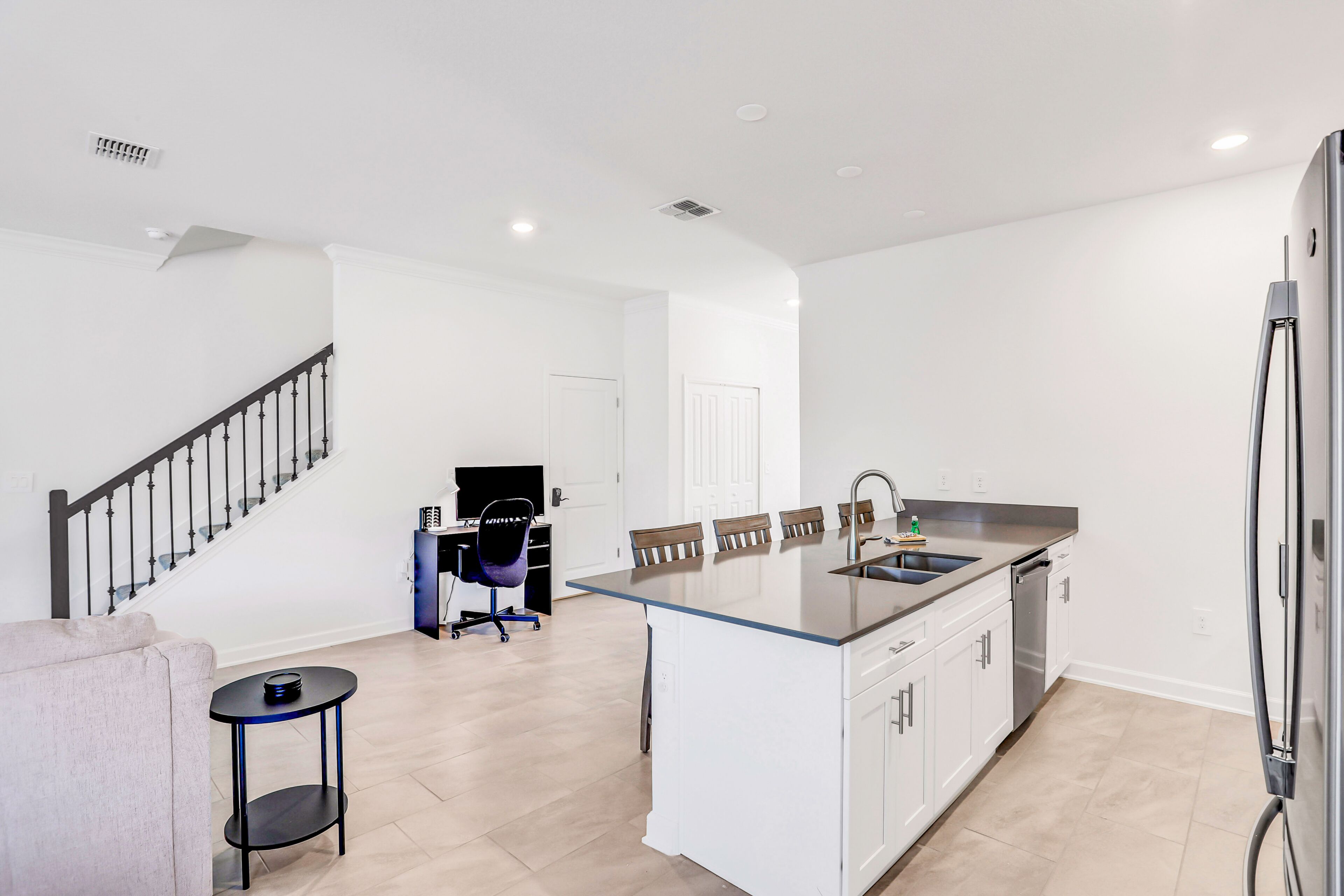 Une cuisine moderne avec un îlot central, un coin repas avec des chaises, un escalier et une petite table d’appoint.