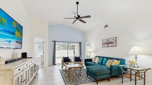 Un salon comprenant un canapé, une table basse, un téléviseur, un ventilateur de plafond et une vue sur l’extérieur, visible à travers une porte vitrée.