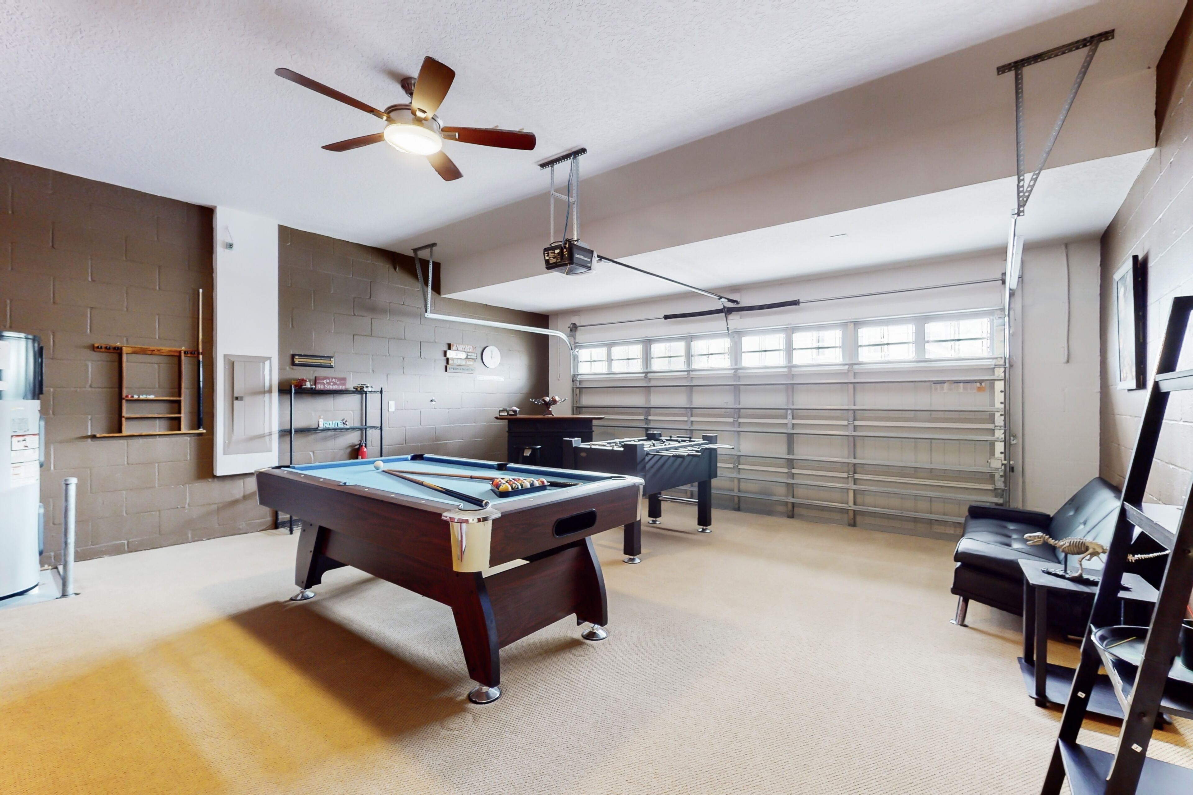 A pool table in a room with a ceiling fan, a projector, and a garage door in the background.