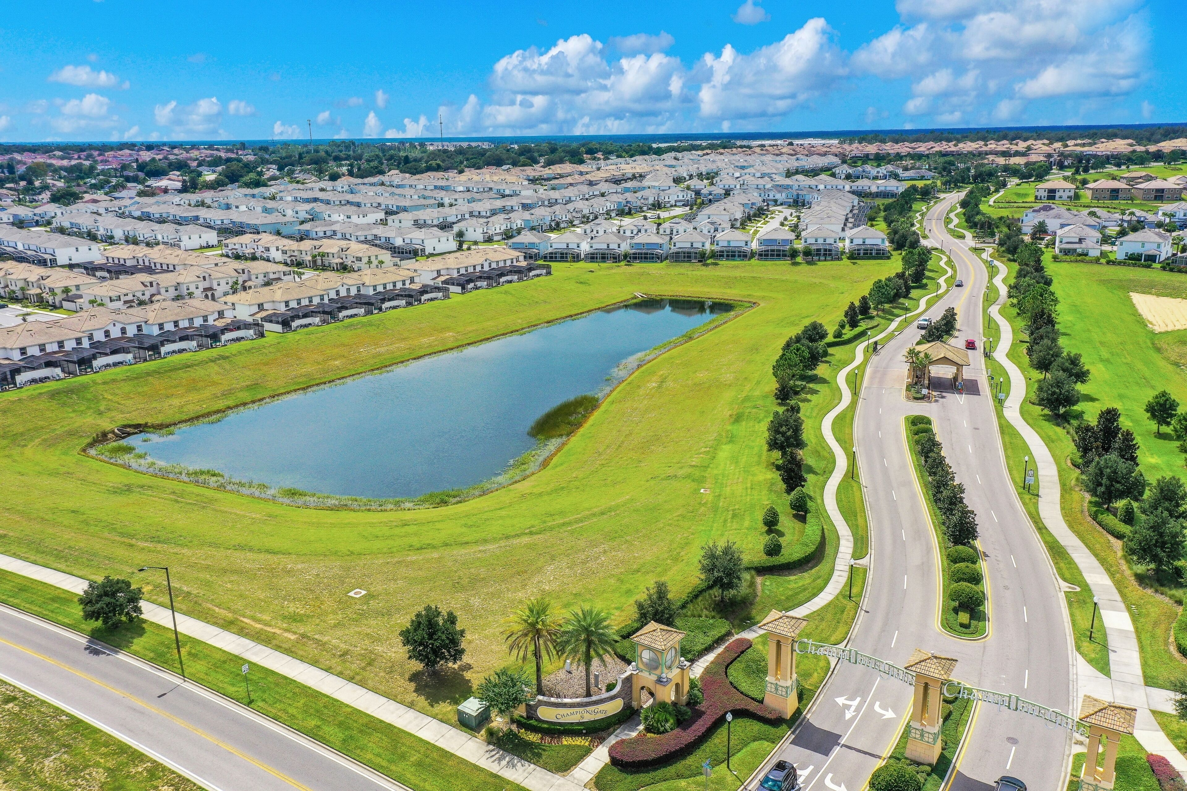 Vue aérienne d’un quartier résidentiel avec un grand étang, une route sinueuse et une entrée fermée par un portail.