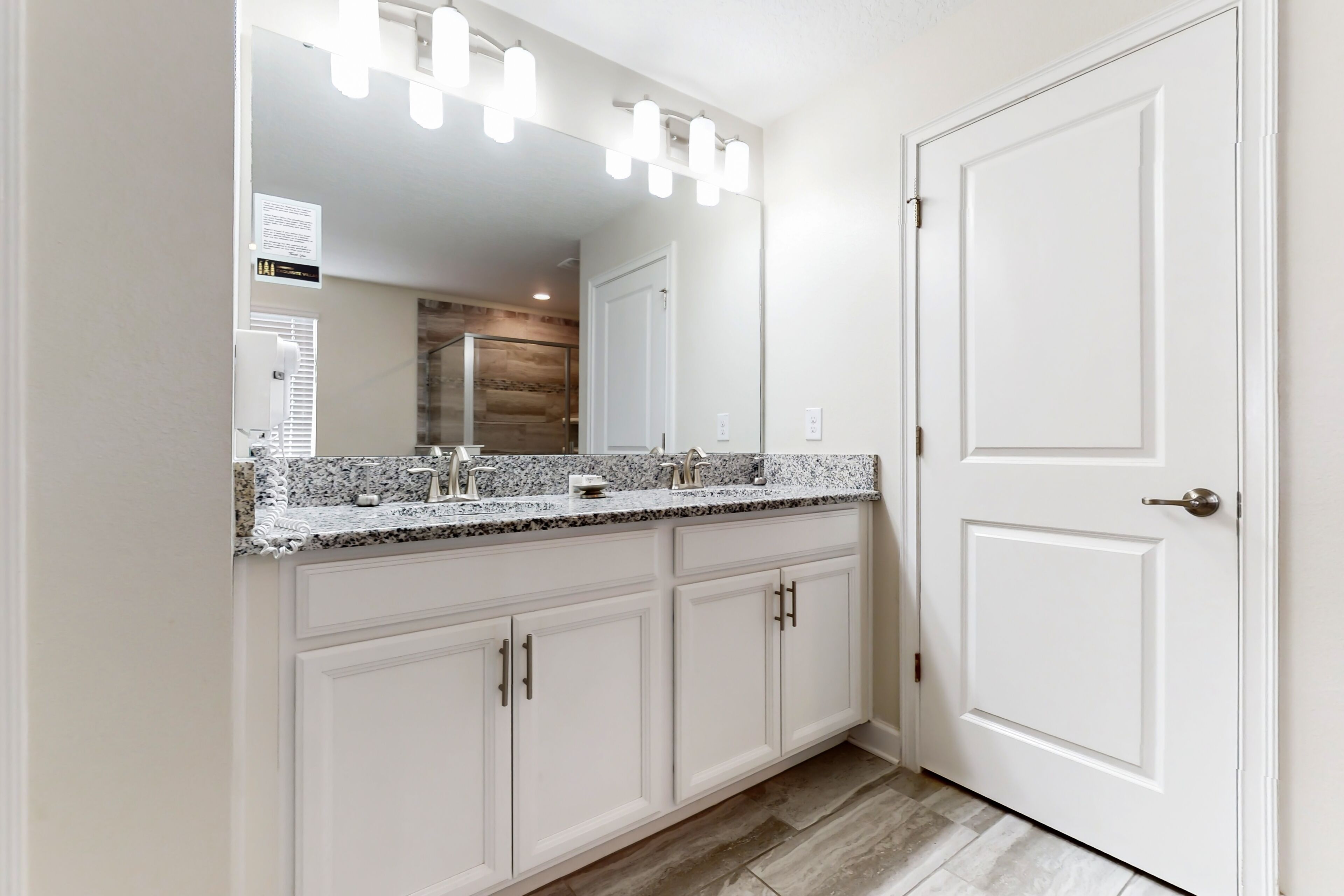 A bathroom with a granite countertop, white cabinets, and a large mirror with lights.