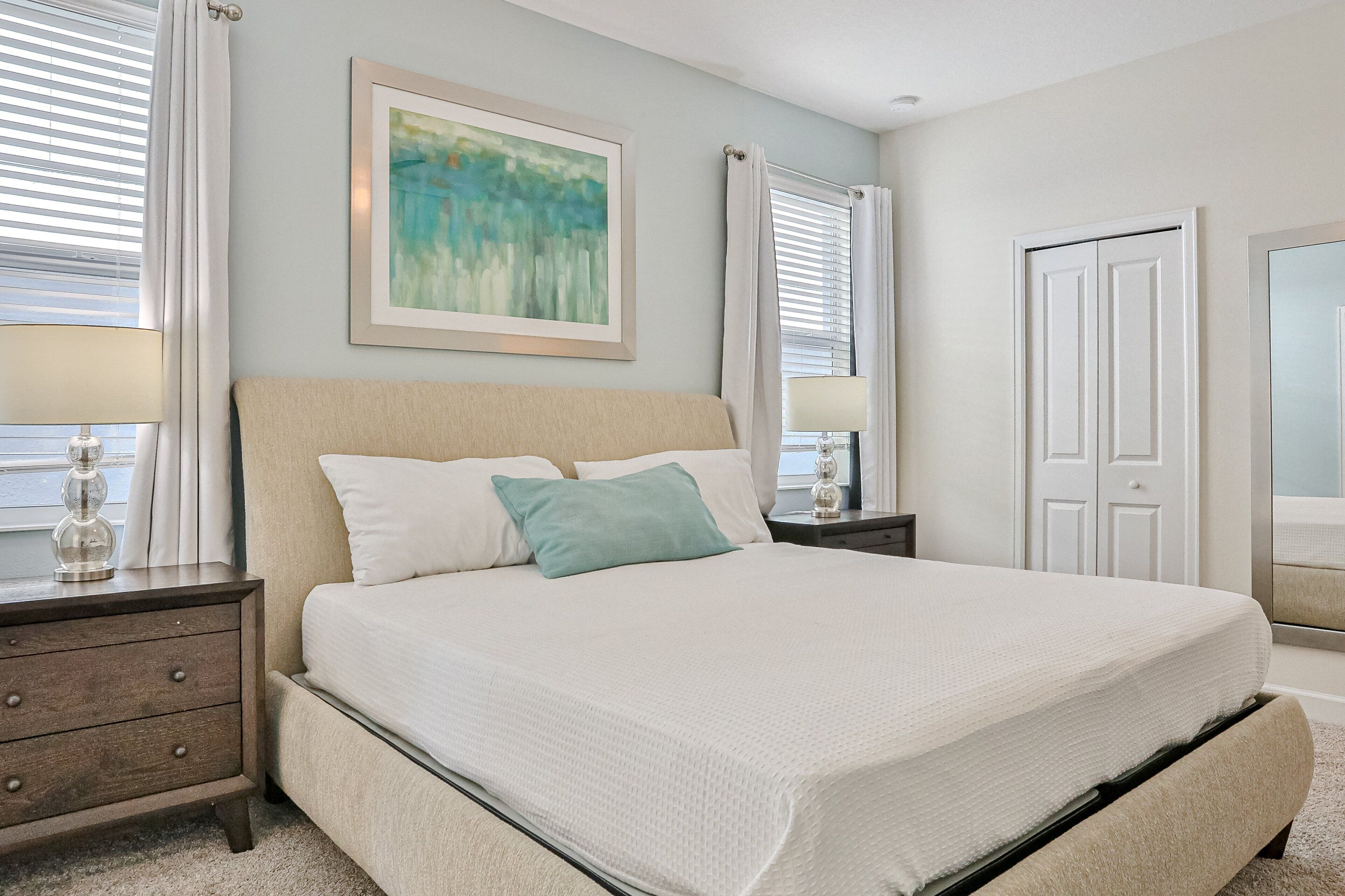 A bedroom with a bed, nightstands, a framed painting, and a door.