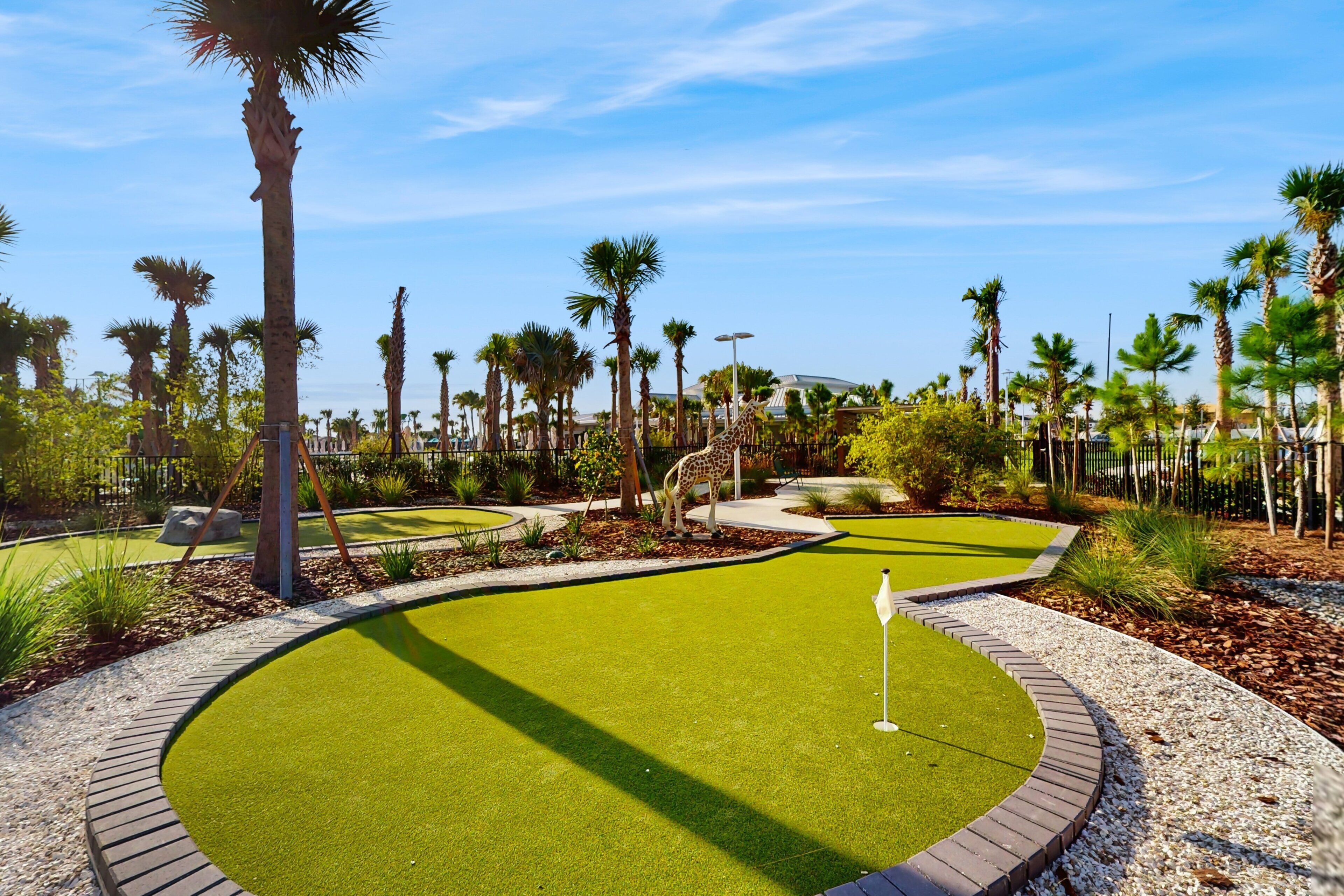 A golf course with a putting green, palm trees, and a giraffe statue.