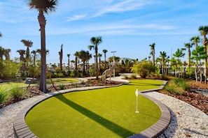 Een golfbaan met een putting green, palmbomen en een girafbeeld.