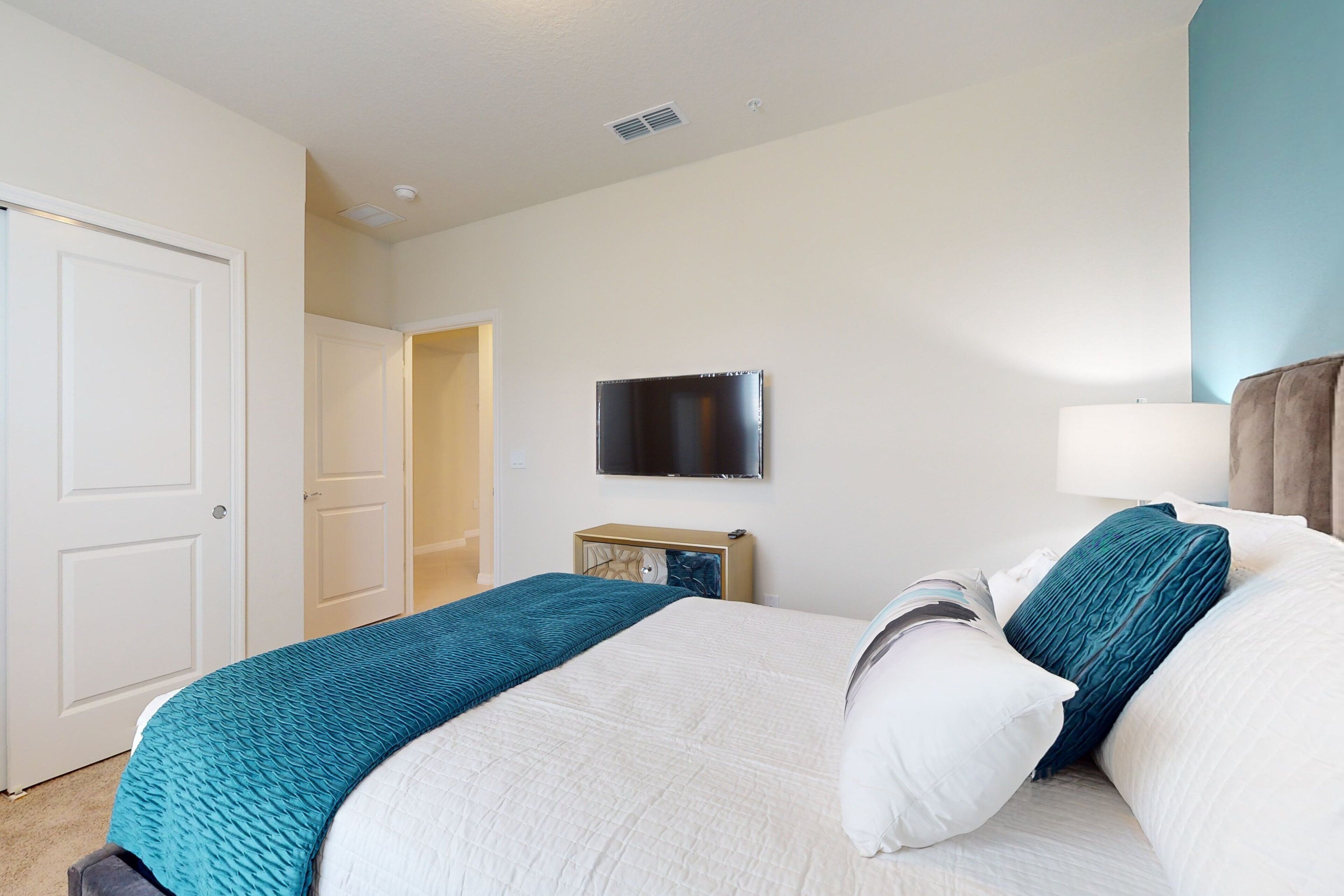 Une chambre à coucher avec un lit, un téléviseur fixé au mur, une table de chevet et une porte.
