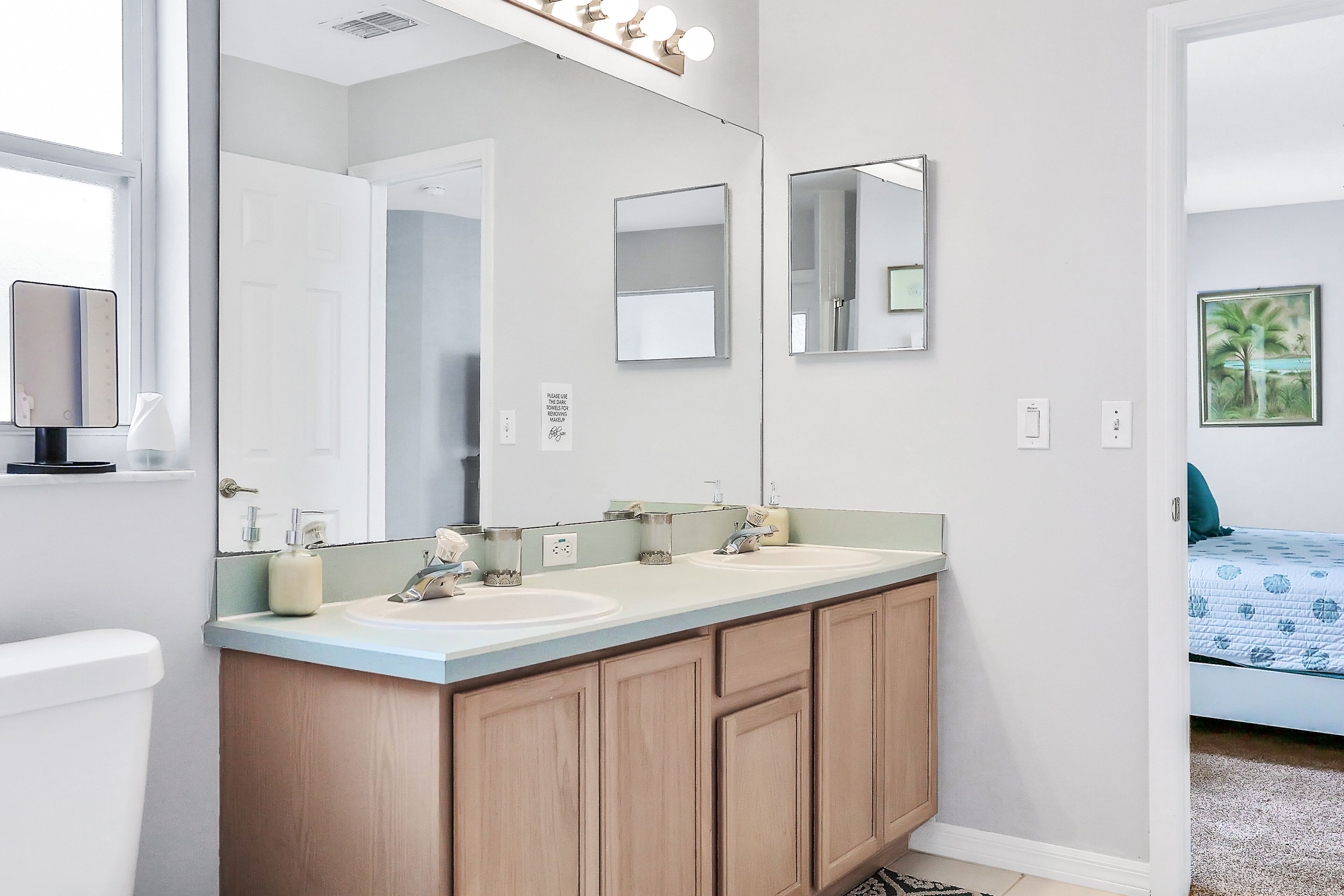 Une salle de bain avec un meuble-lavabo à deux vasques, un grand miroir et un luminaire placé au-dessus du miroir.