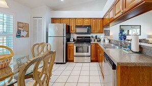 A kitchen with wooden cabinets, stainless steel appliances, a granite countertop, and a dining area with glass-top table and wooden chairs. - Dog-friendly Getaway With Private Pool, Tennis & AC - Near Theme Parks (Davenport)