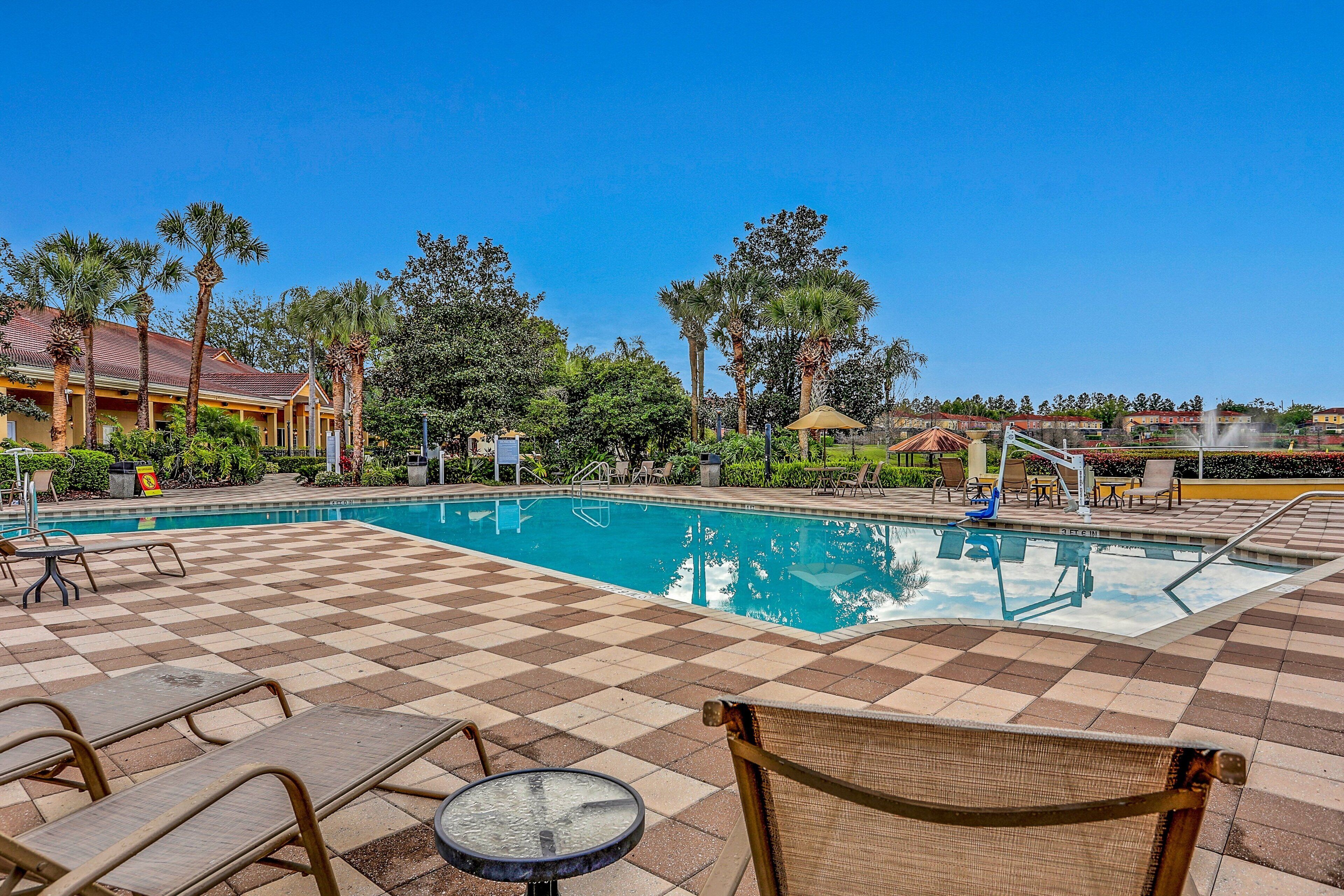A pool area with checkered flooring, lounge chairs, and palm trees.