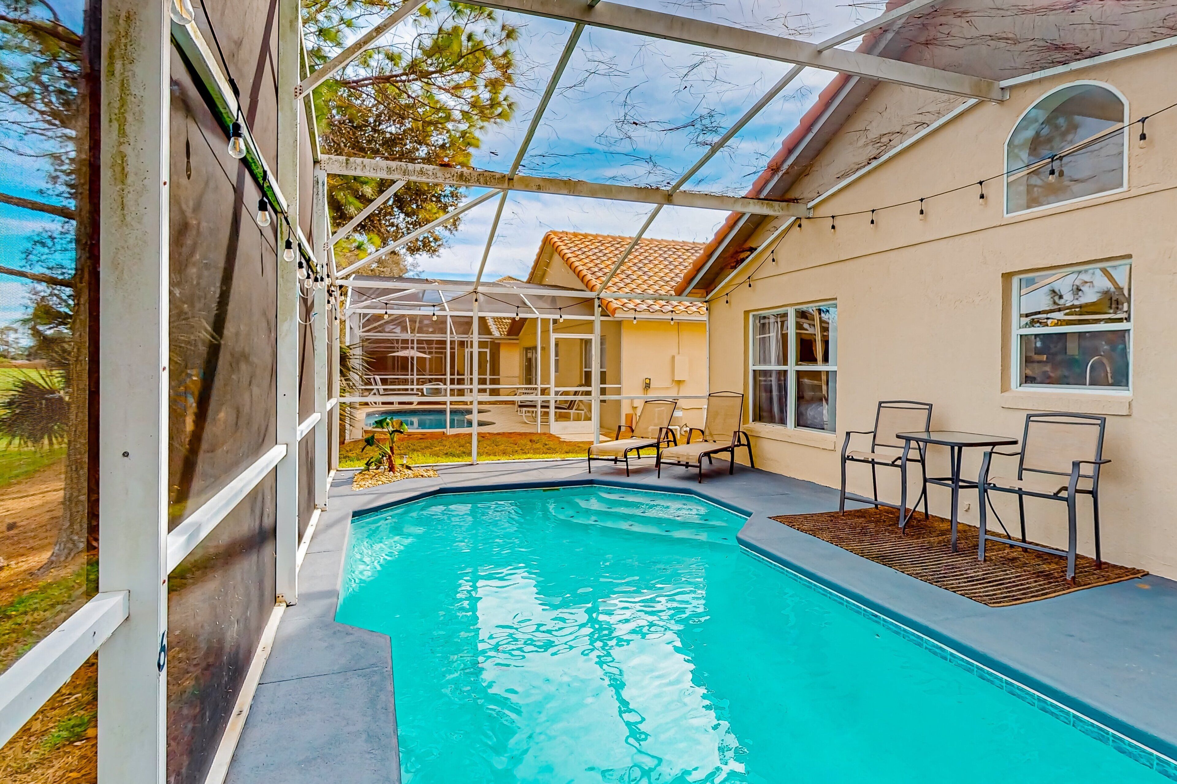 Ein Schwimmbad mit überdachter Terrasse, Sitzgelegenheiten im Freien und Blick auf das Haus.